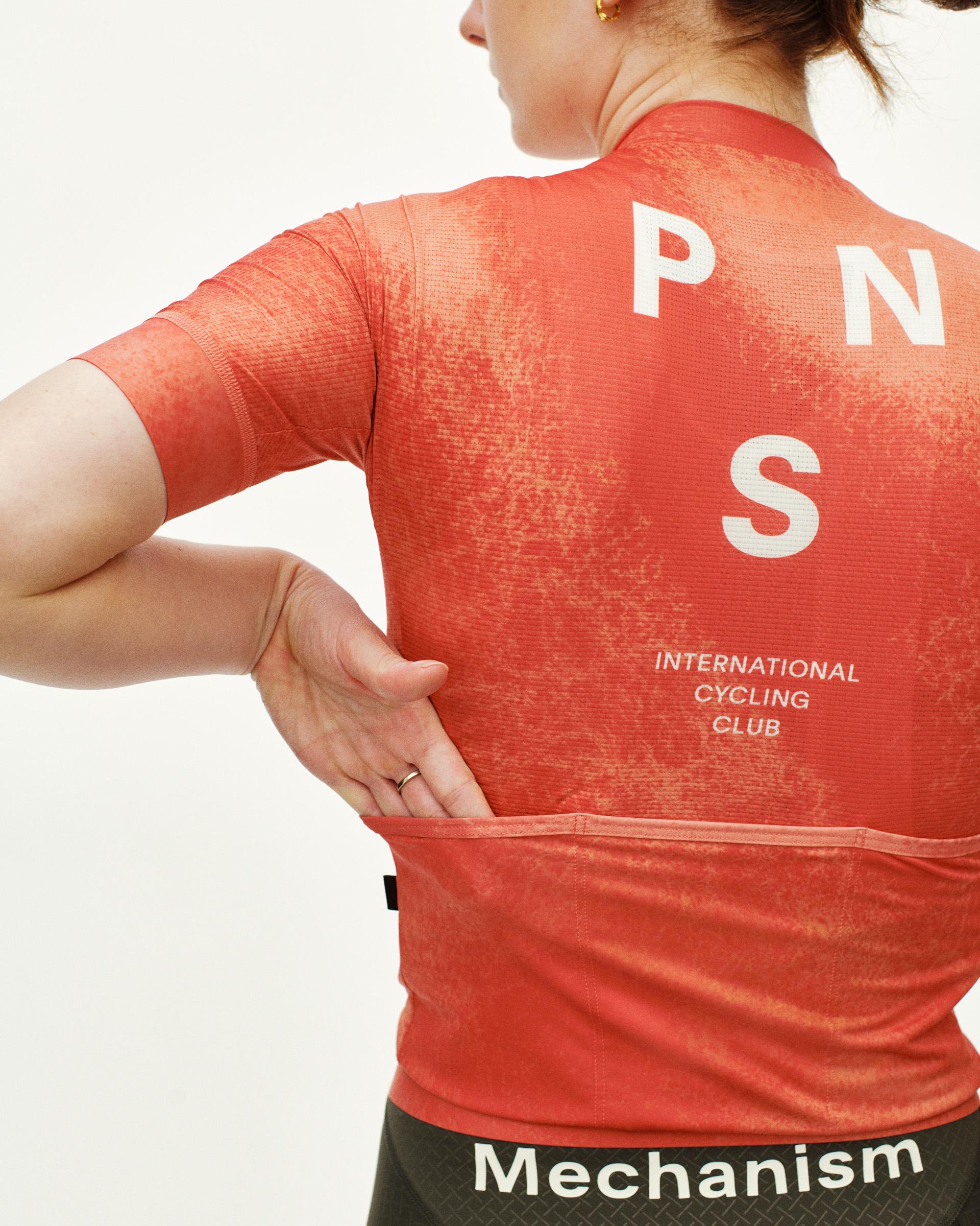 Orange Mechanism cycling jersey on model, rear view with white PNS logo and International Cycling Club text