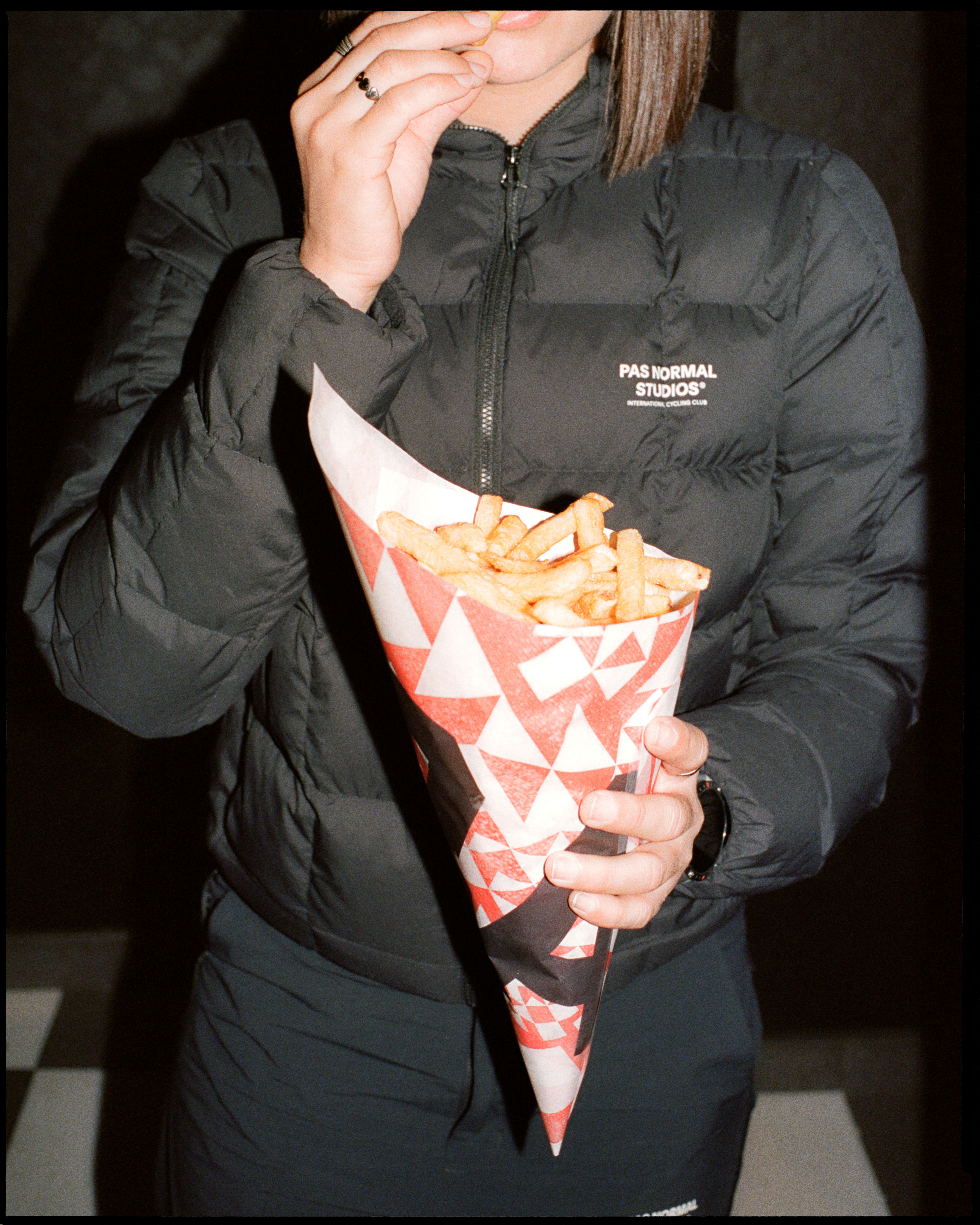 Model wearing black quilted down jacket with chest logo holding french fries
