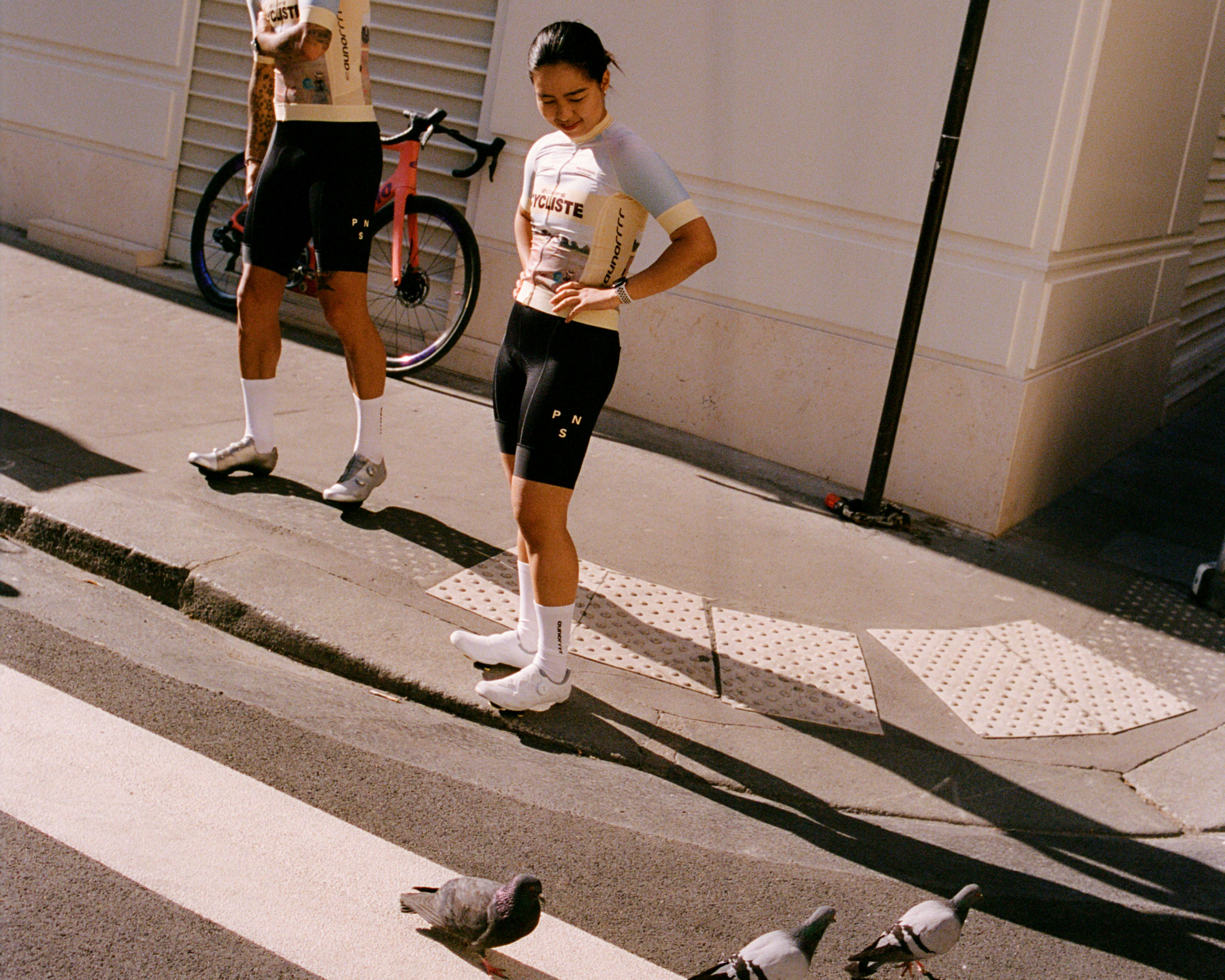 Models wearing white jerseys with text and black shorts on urban street with bicycle