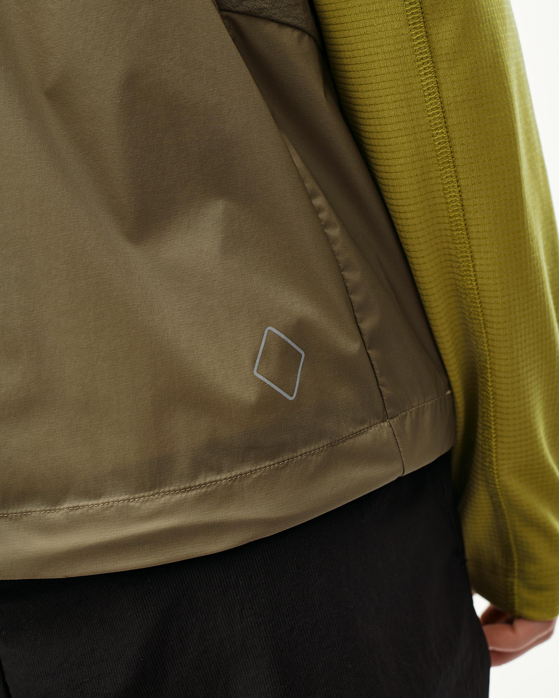 Dusty Earth khaki Balance Windproof Vest on model, side detail with reflective diamond logo and contrast ribbed sleeve
