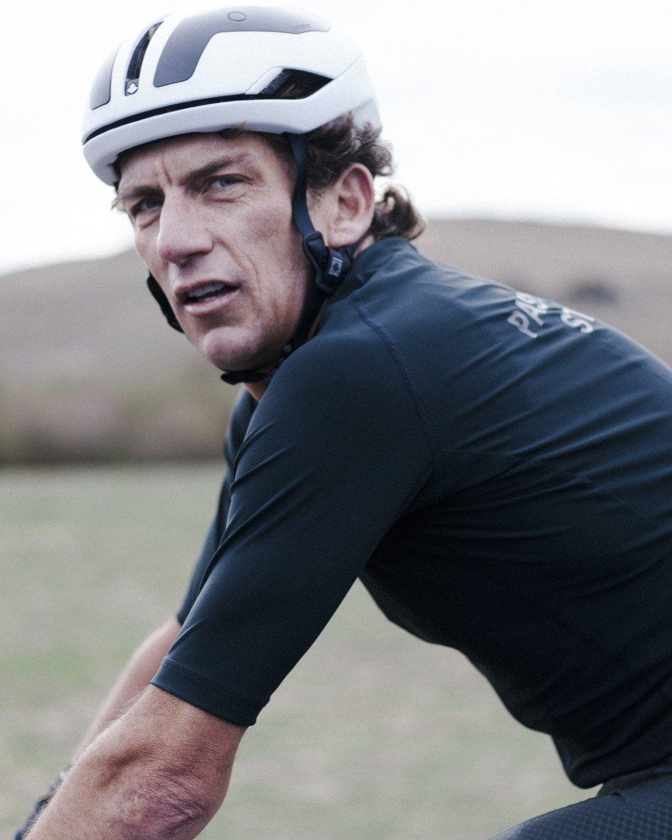 Model wearing dark blue cycling jersey with white helmet in outdoor setting