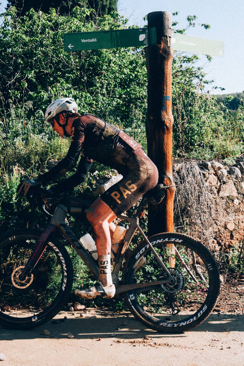 Model wearing PAS collection cycling kit on mountain bike at trail marker