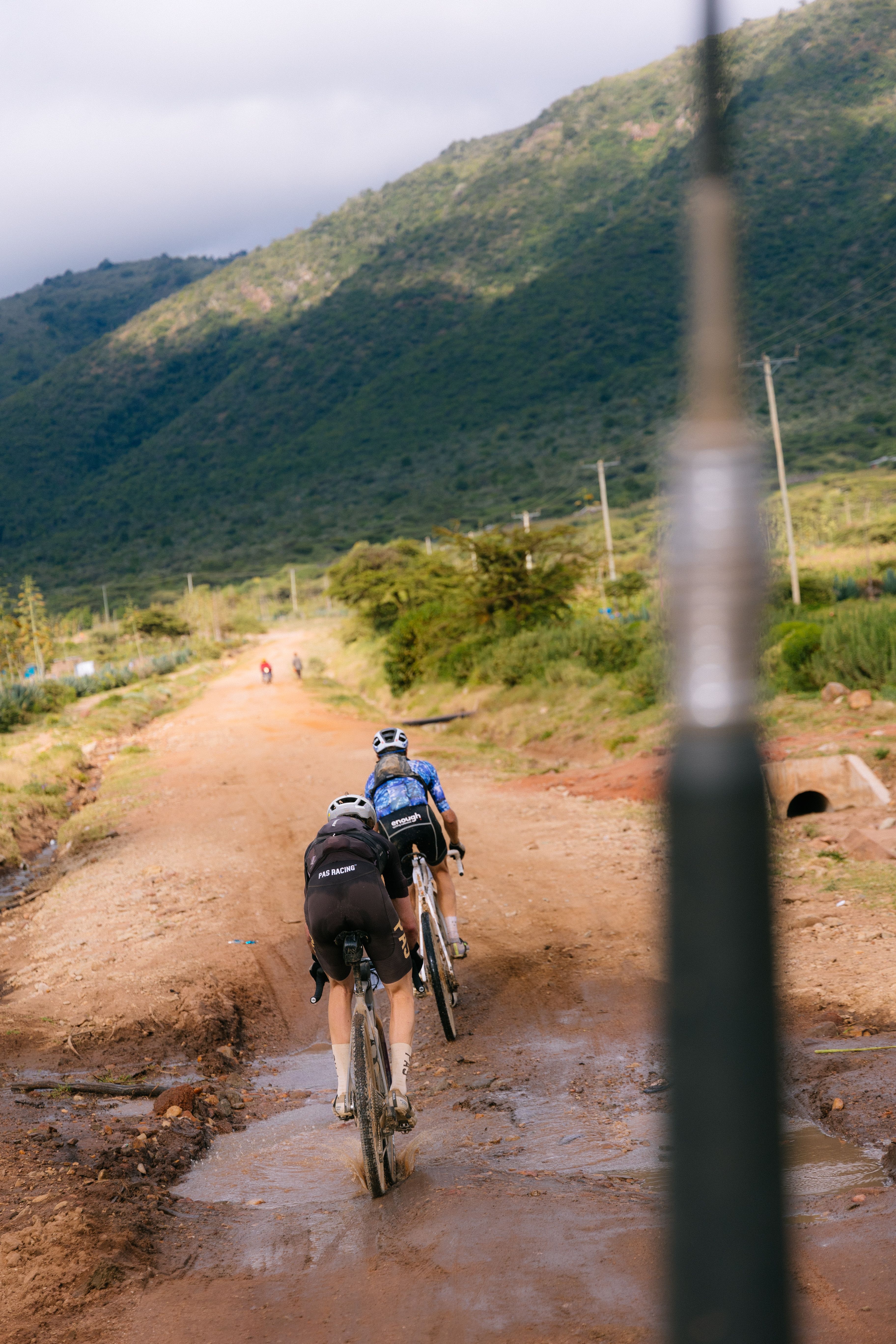 Cyclists riding gravel bikes on dirt road through hilly countryside landscape