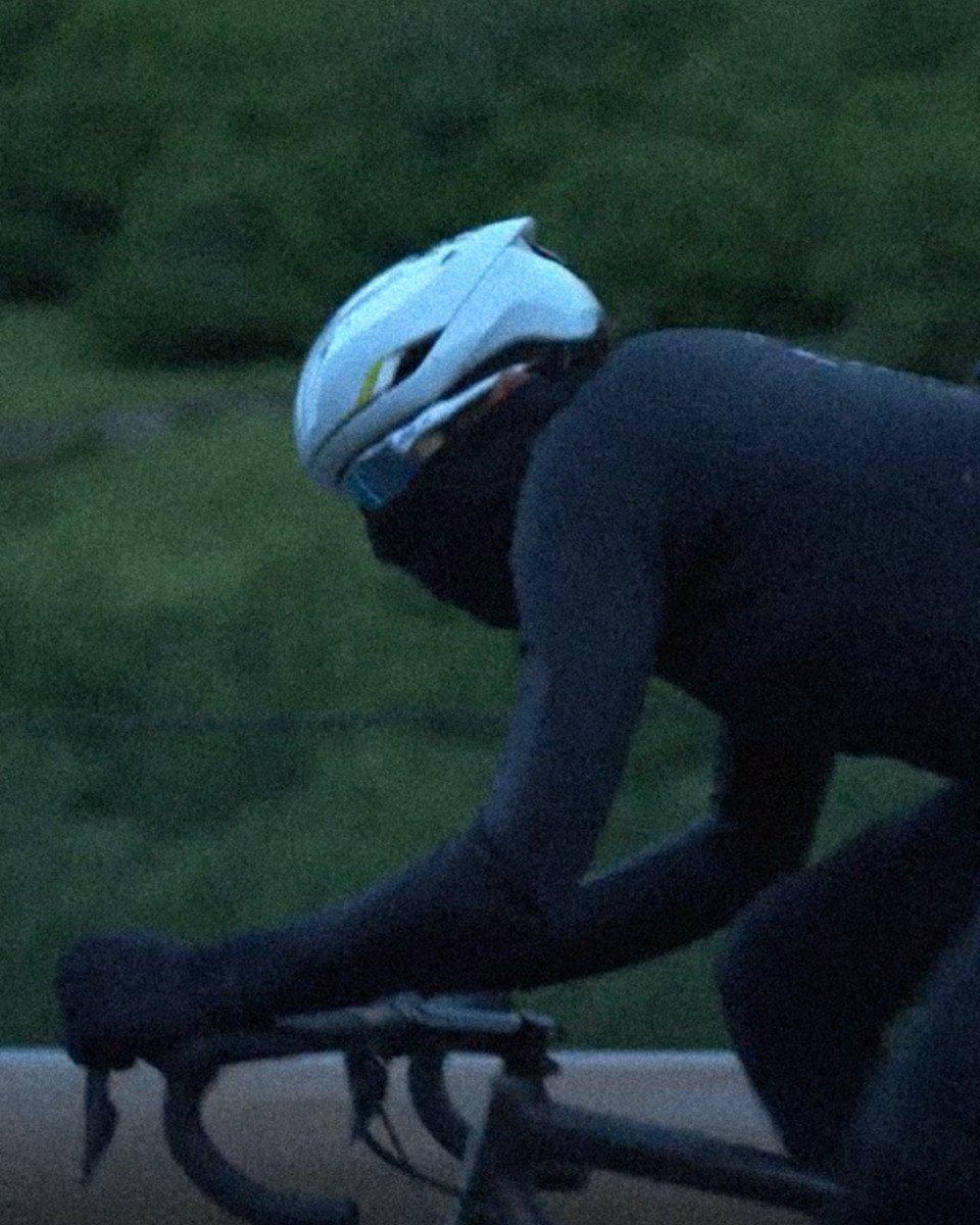 Model wearing dark cycling outfit with white helmet in aerodynamic position on bike