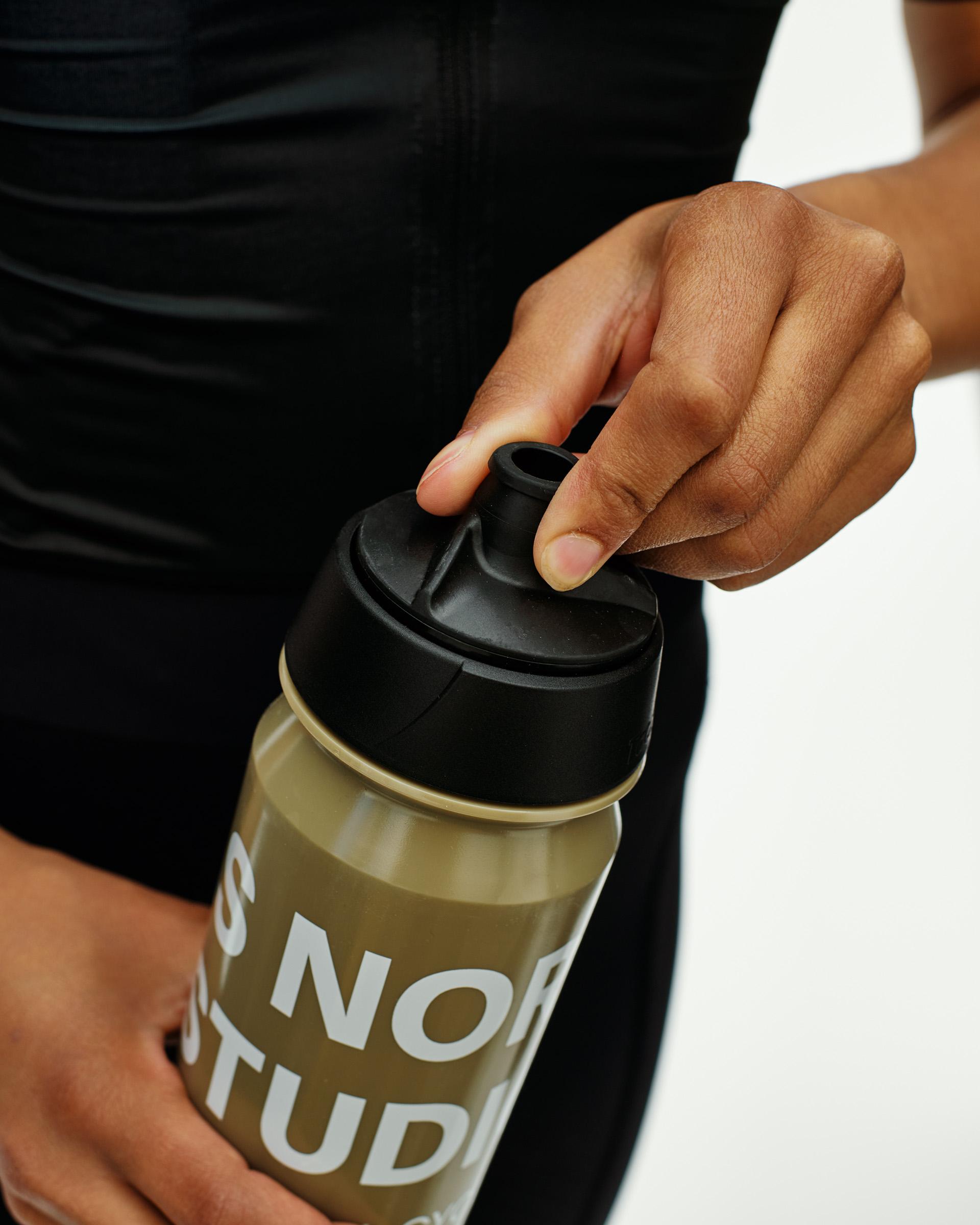 Beige Essential Logo Bidon cycling water bottle, detail view on model with black cap