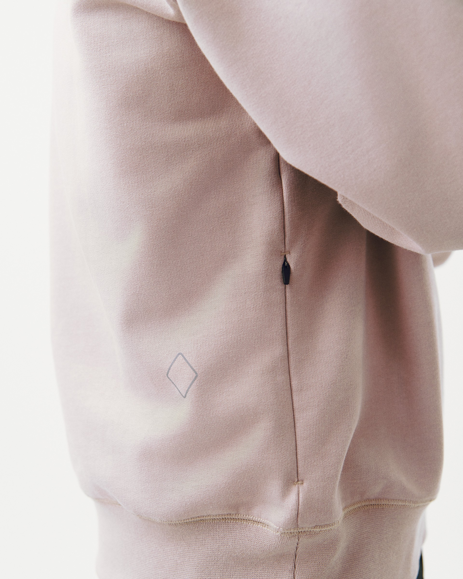 Small zippered pocket integrated into side seam of beige sweatshirt with diamond logo
