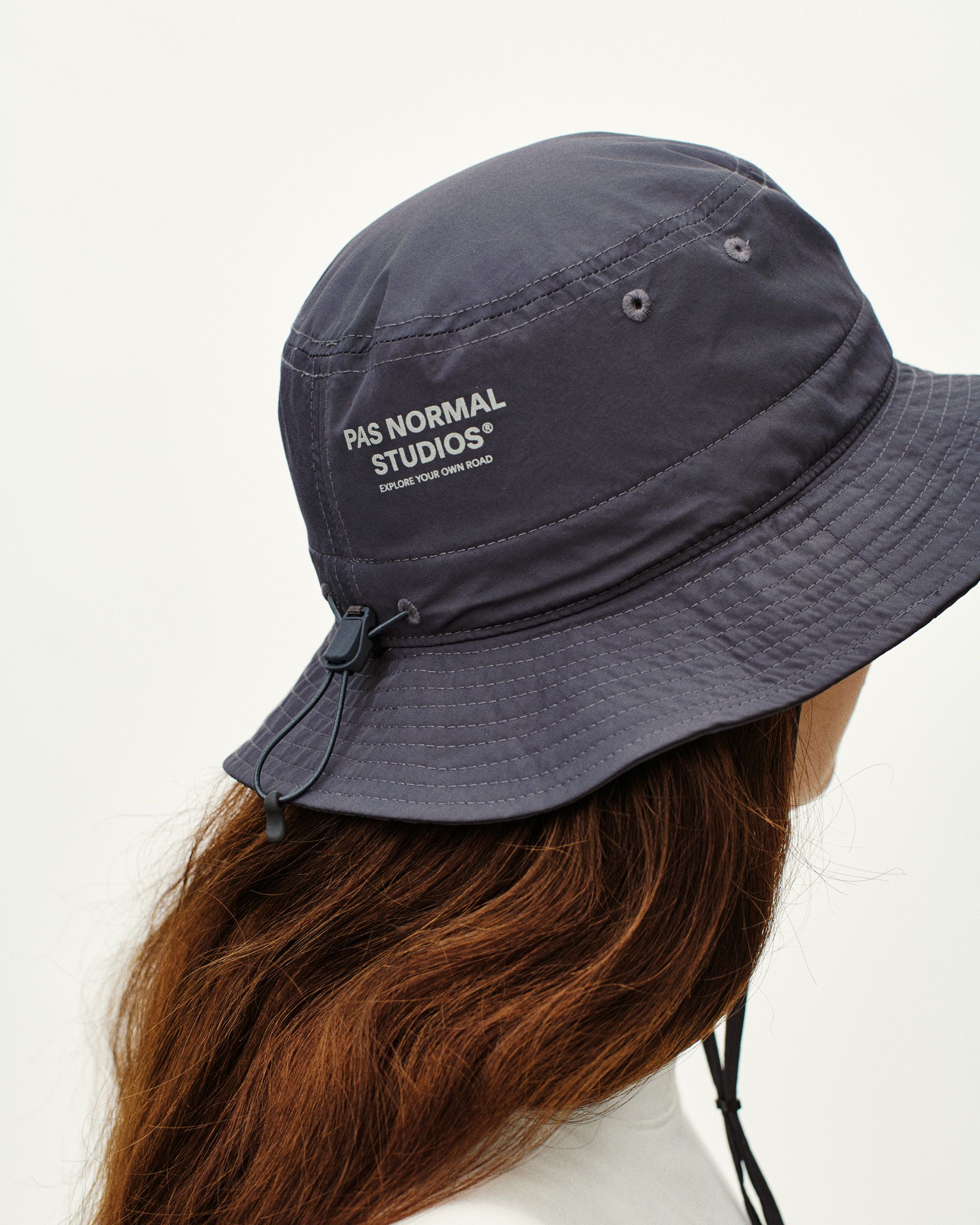 Steel Off-Race Tech bucket hat on model, side view with chin strap and white logo print