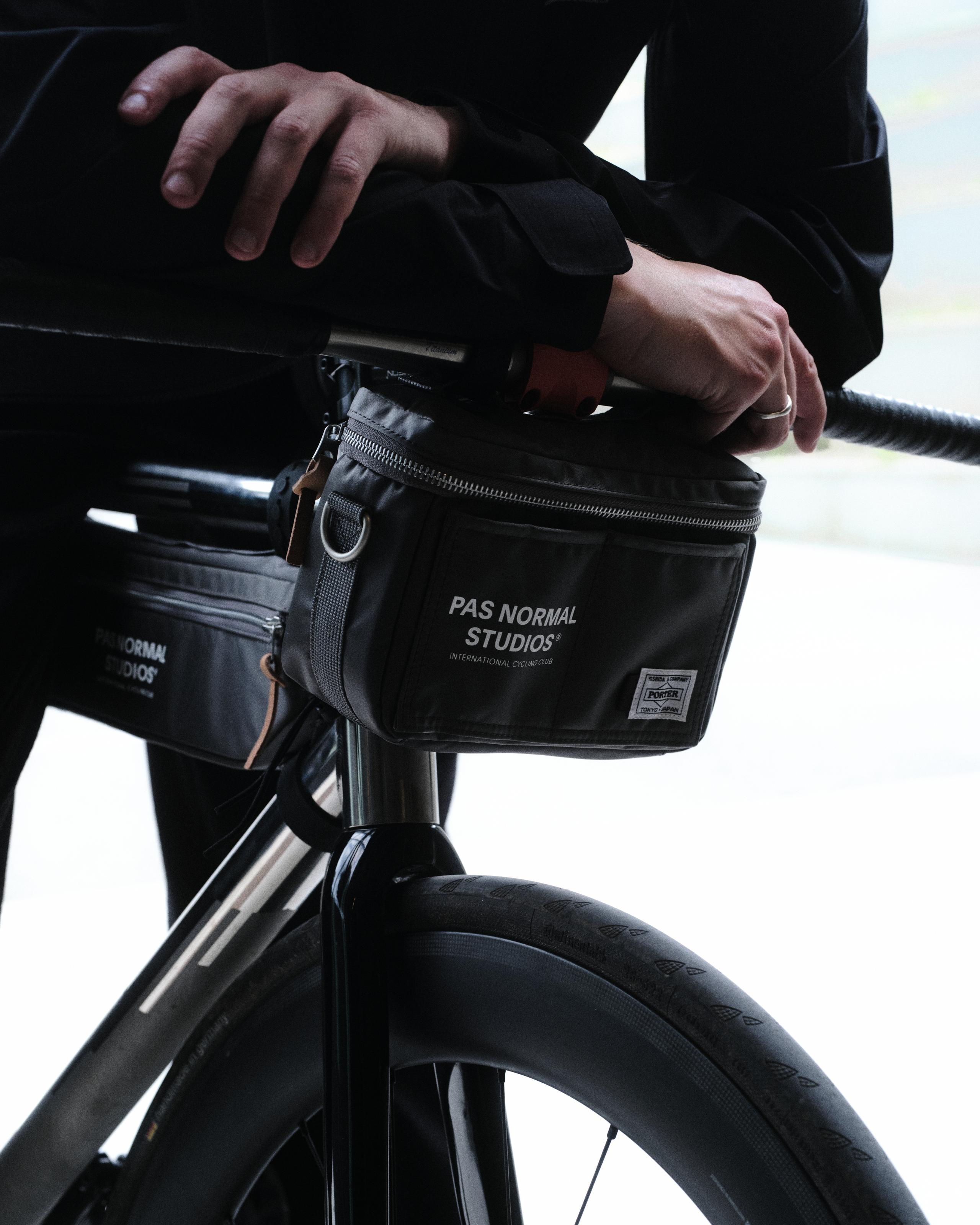 Black frame bag mounted on bike handlebars with zipper closure and brand logo