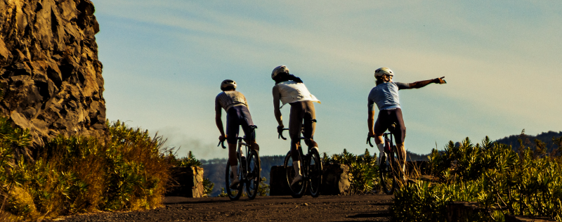 Three cyclists on road bikes pointing and looking out over scenic landscape with rock formations