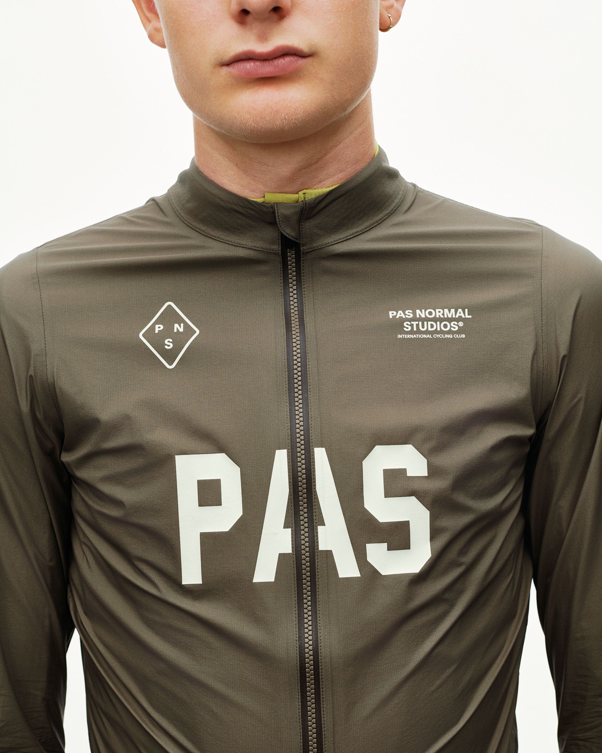 Dark Earth khaki PAS Mechanism Rain cycling jacket on model, front detail with large white PAS chest print