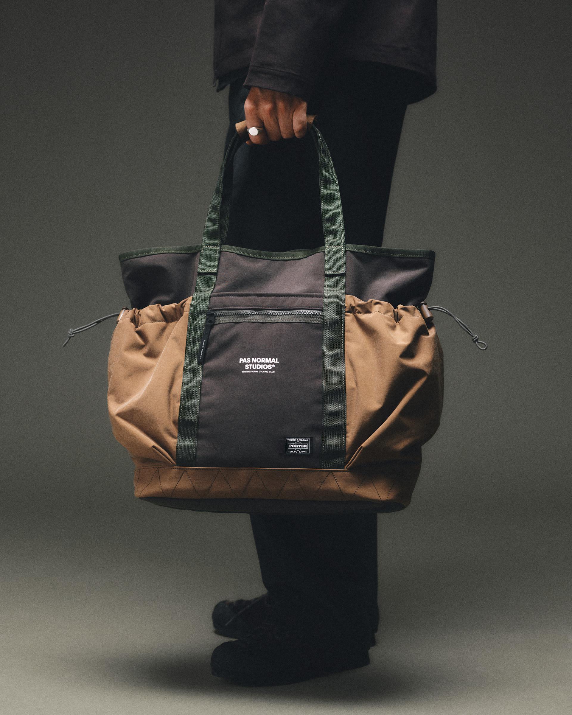 Light Brown Porter-Yoshida tote bag held by model, front view with dark panel, green webbing straps and drawstring sides