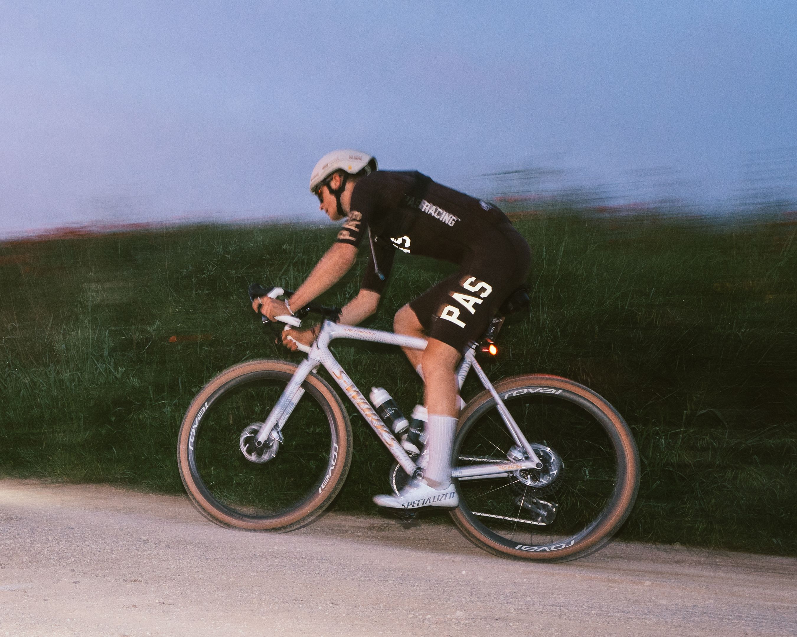 Model wearing black cycling kit with logo racing on time trial bike in countryside