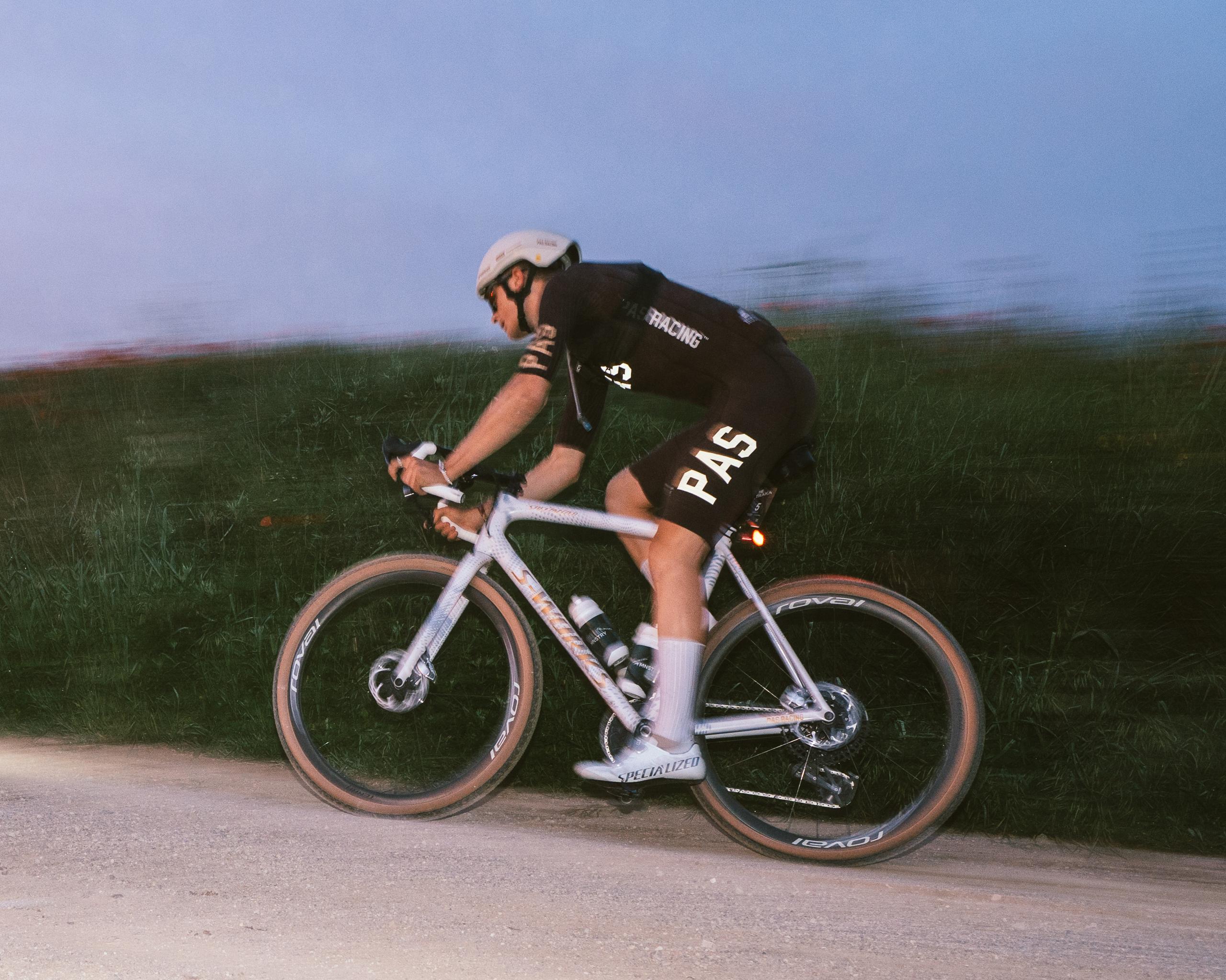 Model wearing black cycling kit with logo racing on time trial bike in countryside