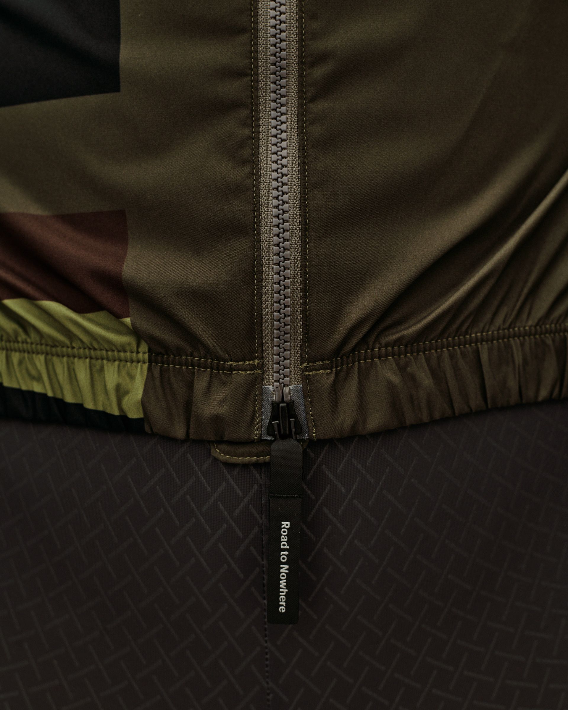 International Green Mechanism Stow Away cycling jacket, front detail view with full zip and branded zip puller