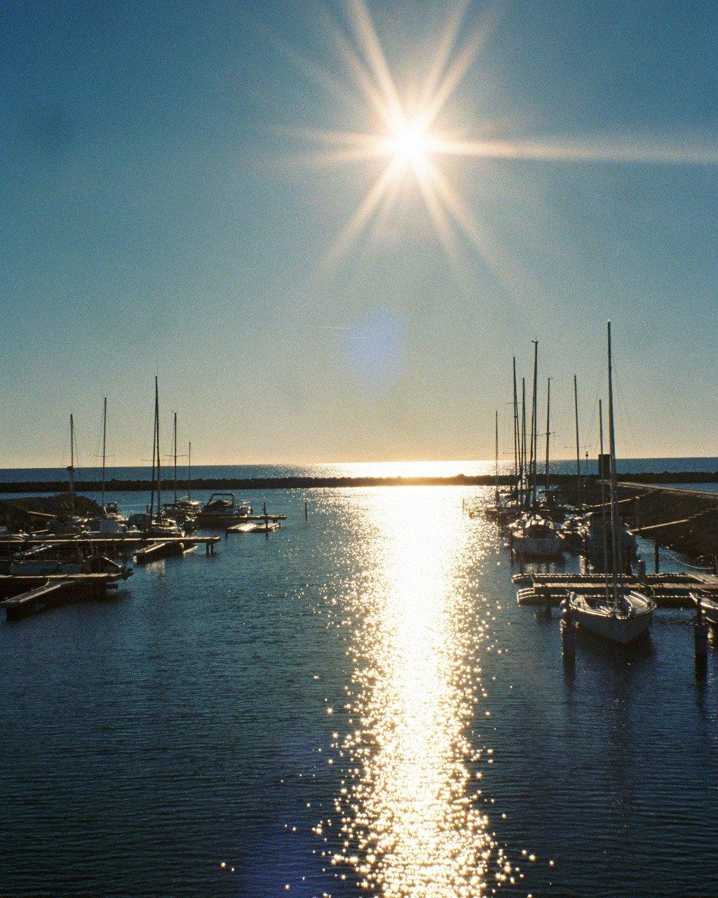 Marina with sailboats at sunset, sun reflecting on water