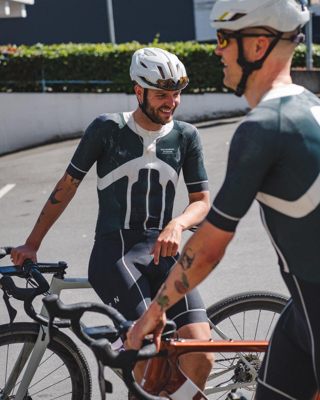 Model wearing Men's Camel 2.0 skinsuit in dark green with white panel design, standing with bike