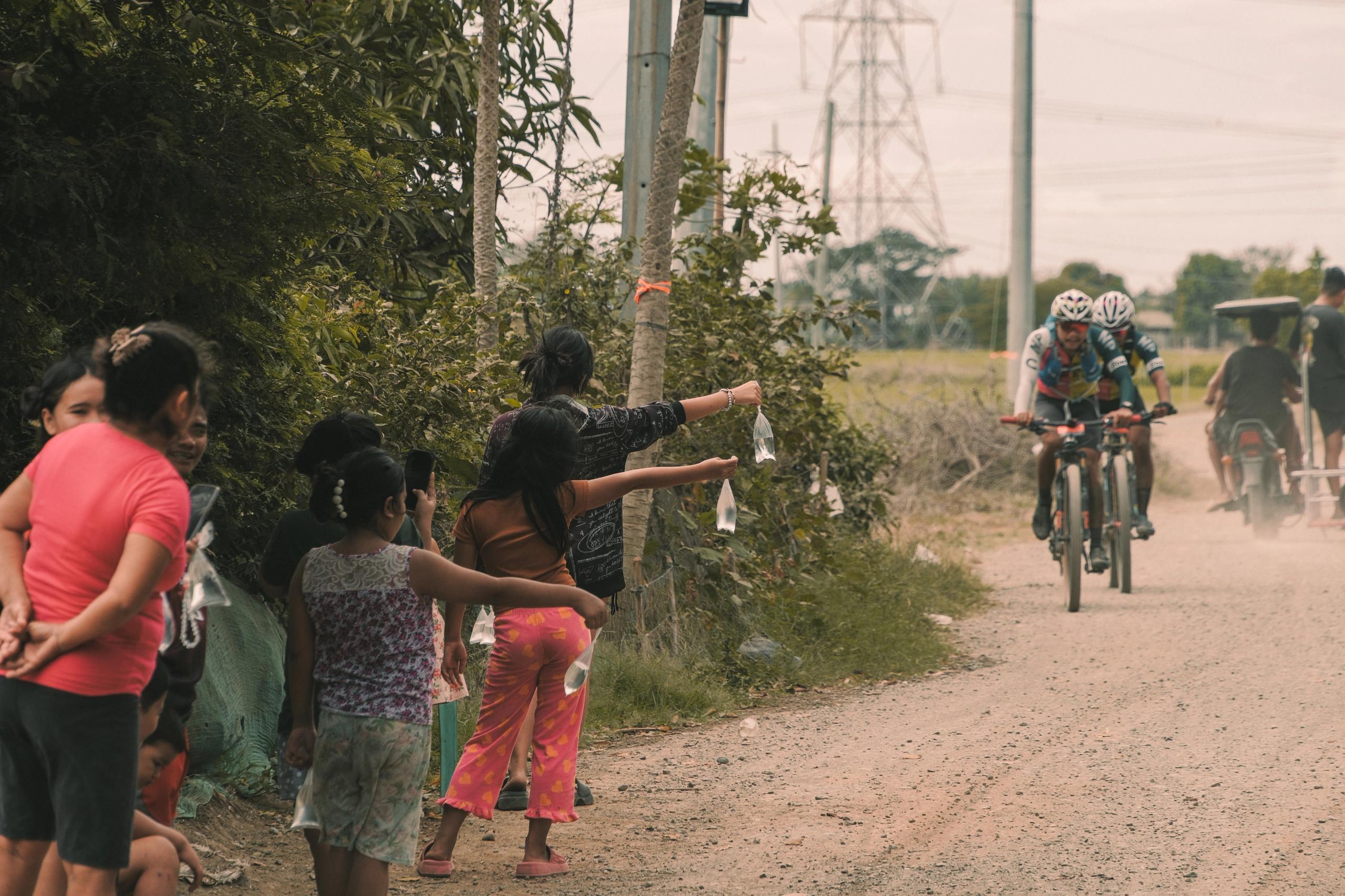 Cyclists racing on gravel road while local spectators cheer from roadside in Philippines