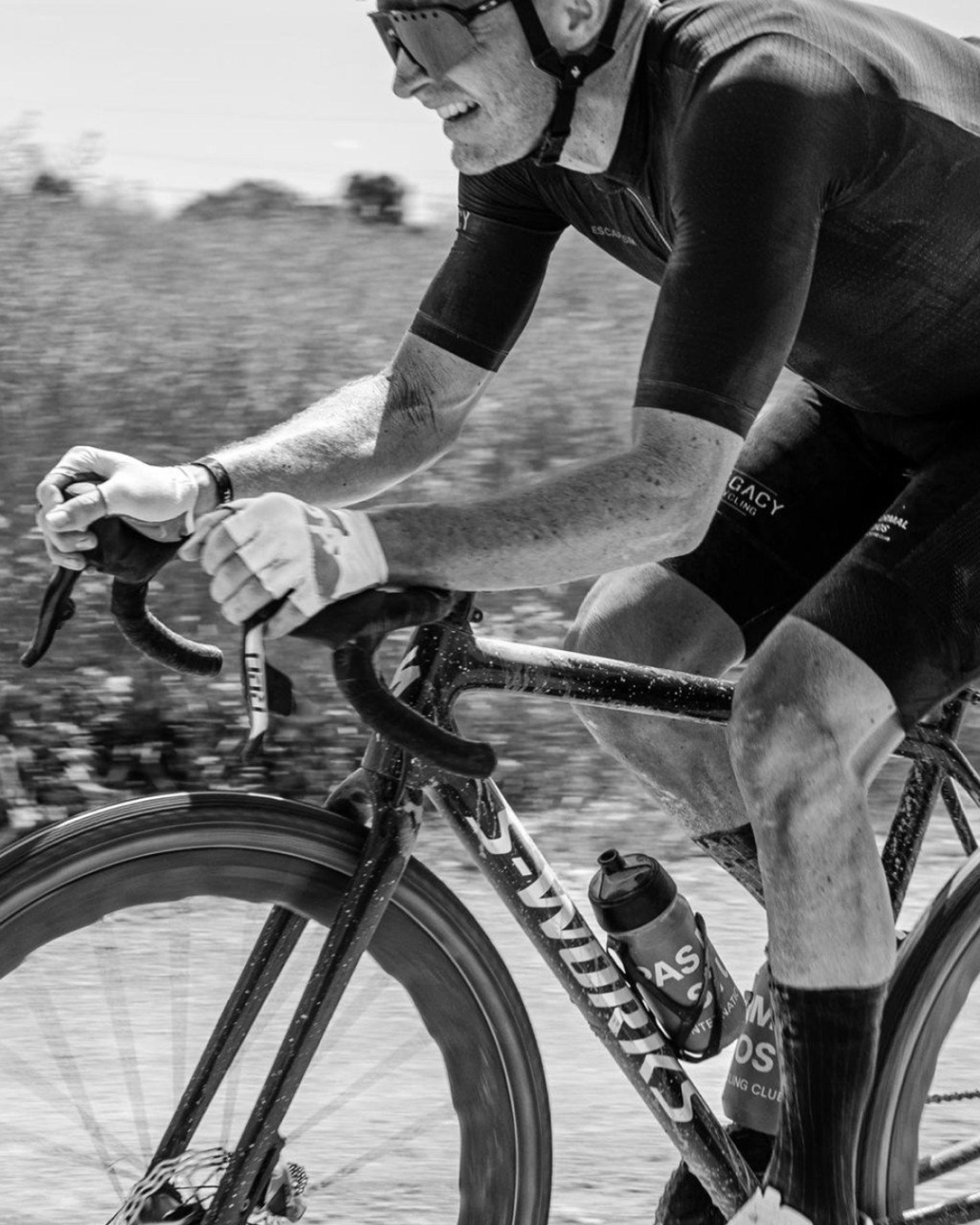 Model wearing black cycling suit with arm warmers in aerodynamic position on time trial bike