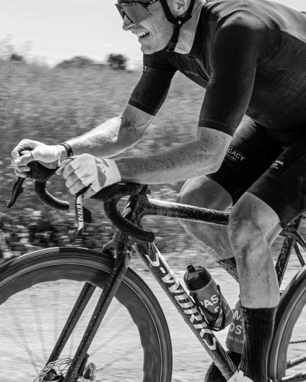 Model wearing black cycling suit with arm warmers in aerodynamic position on time trial bike