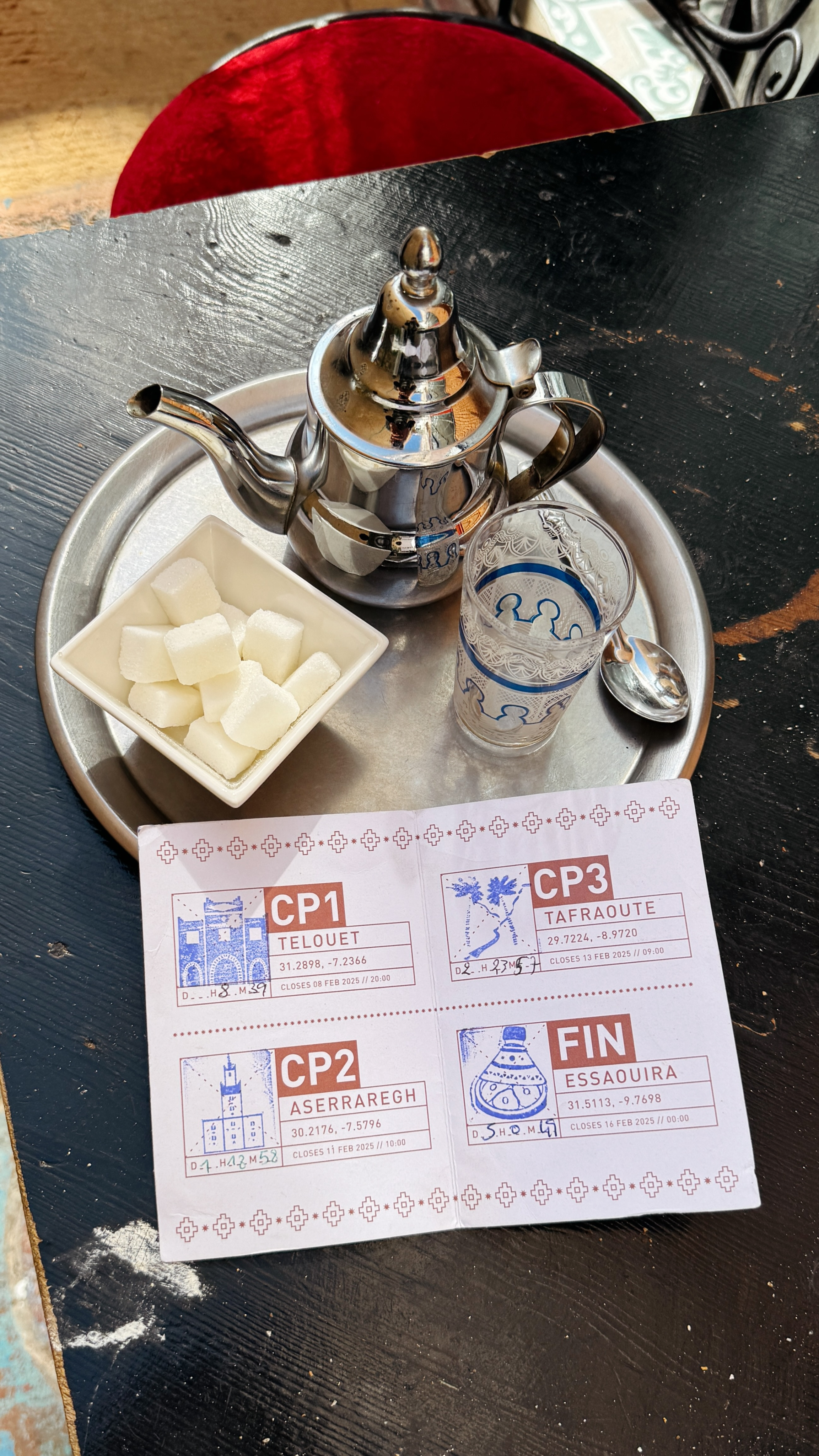 Traditional Moroccan tea service with silver teapot, glass, sugar cubes and Atlas Mountain Race checkpoint card
