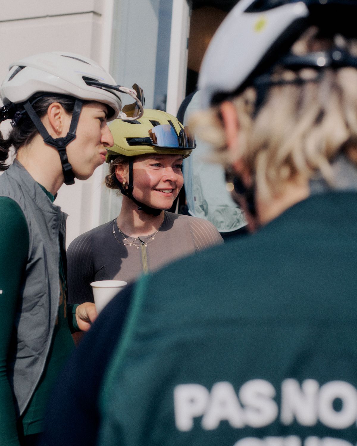 Female cyclists wearing aerodynamic helmets at cycling event with team barrier in foreground