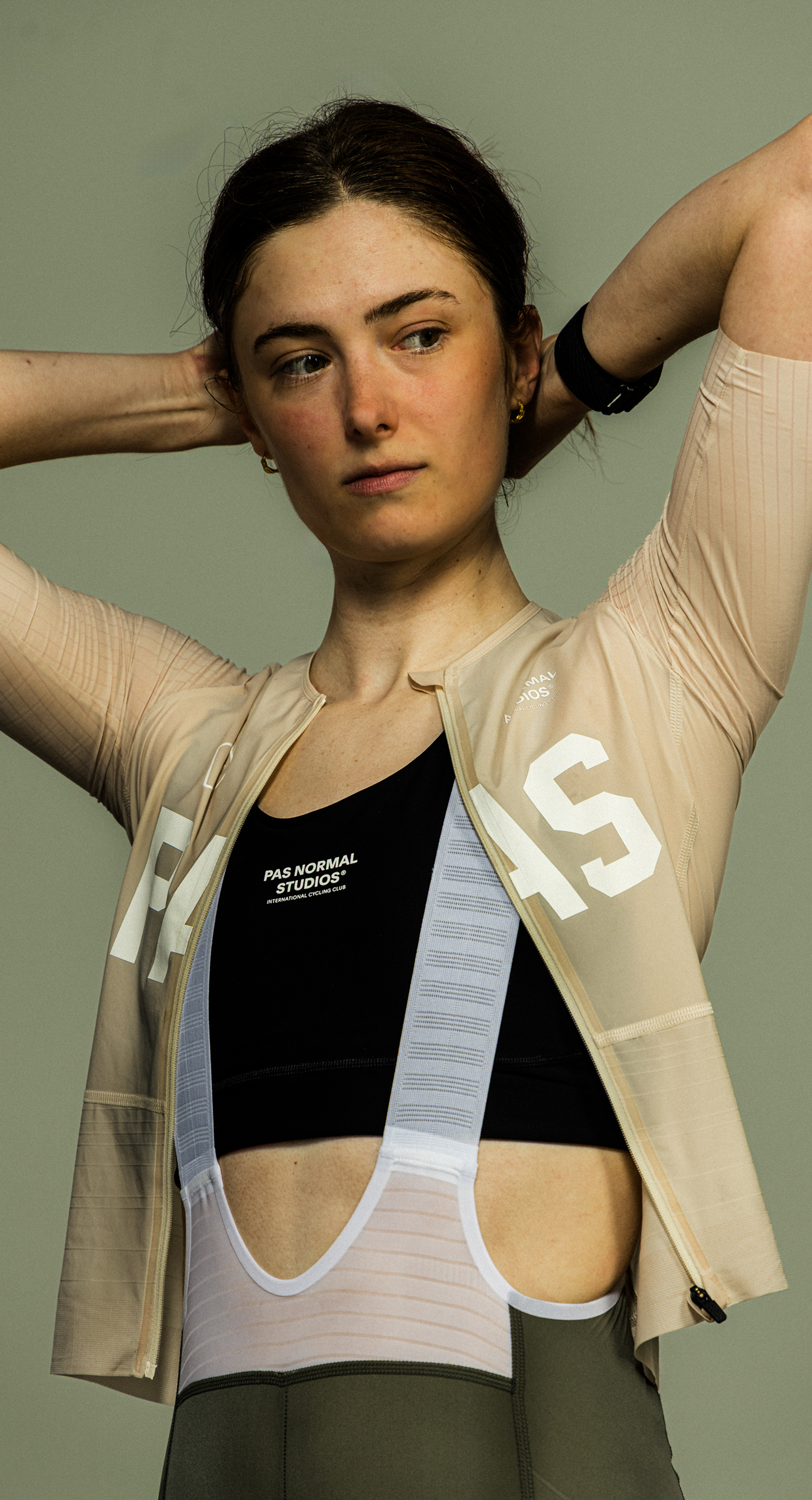 Model wearing Women's beige zip-up jacket with white lettering over black sports bra and white base layer