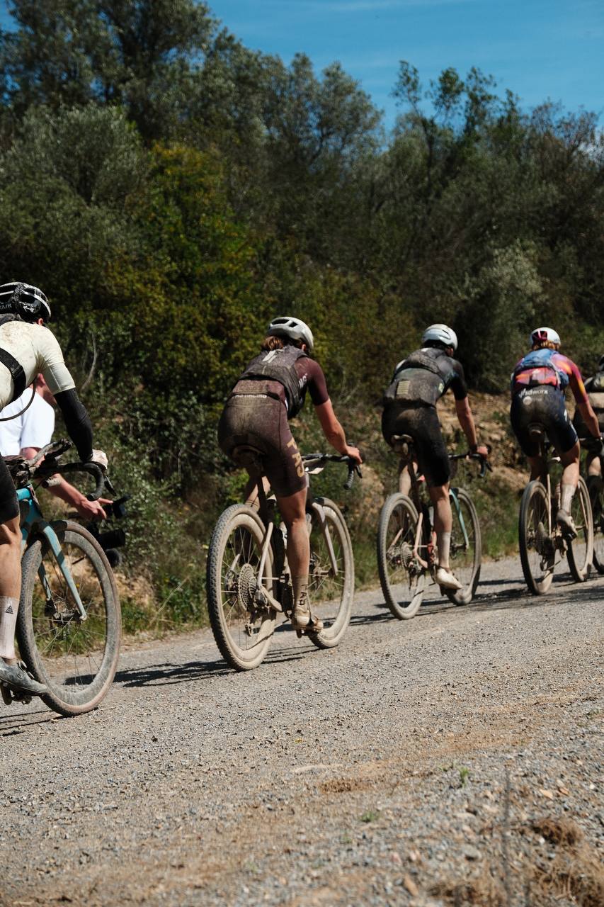Group of cyclists riding gravel bikes on dirt road through wooded countryside