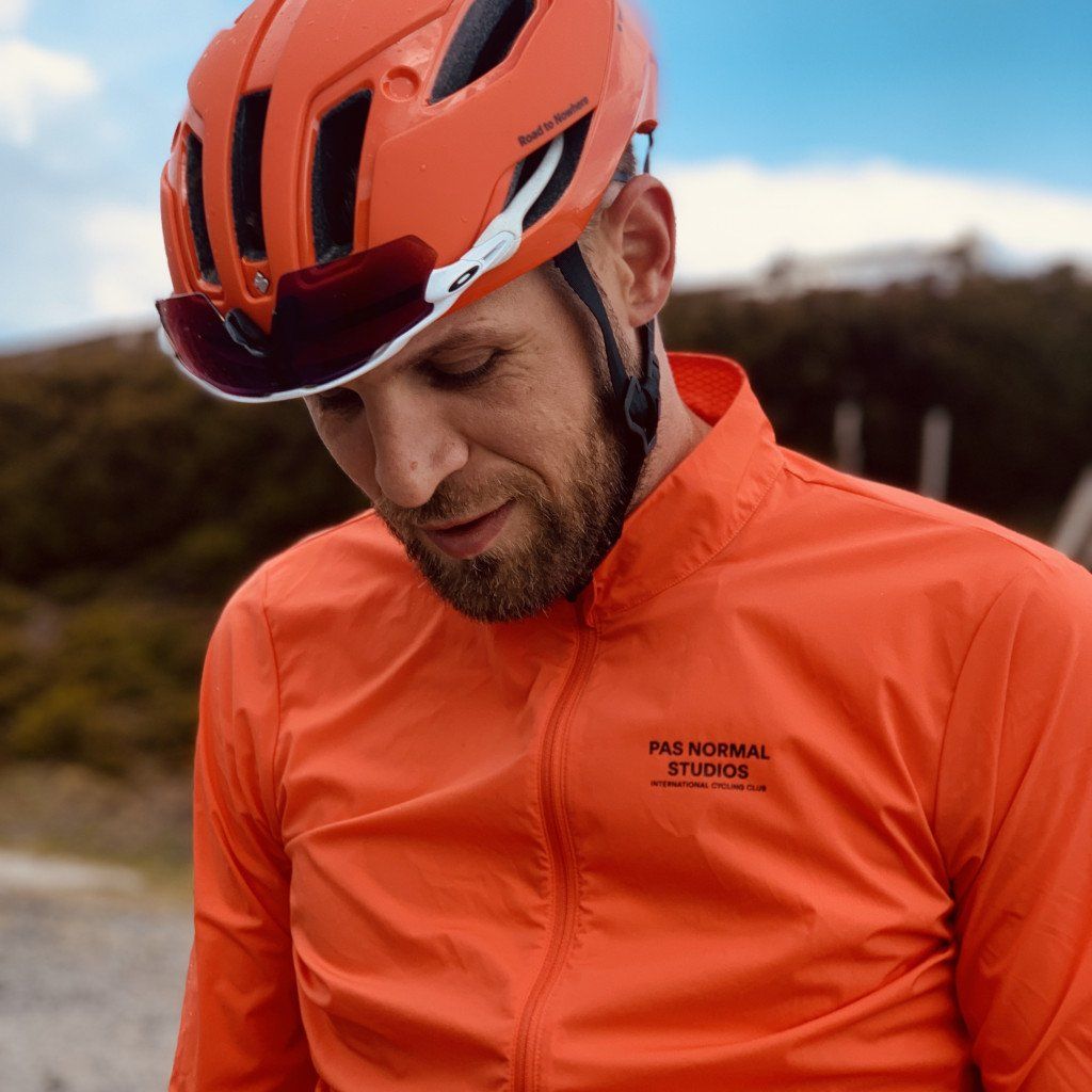 Model wearing orange cycling jacket with chest branding and matching orange helmet outdoors