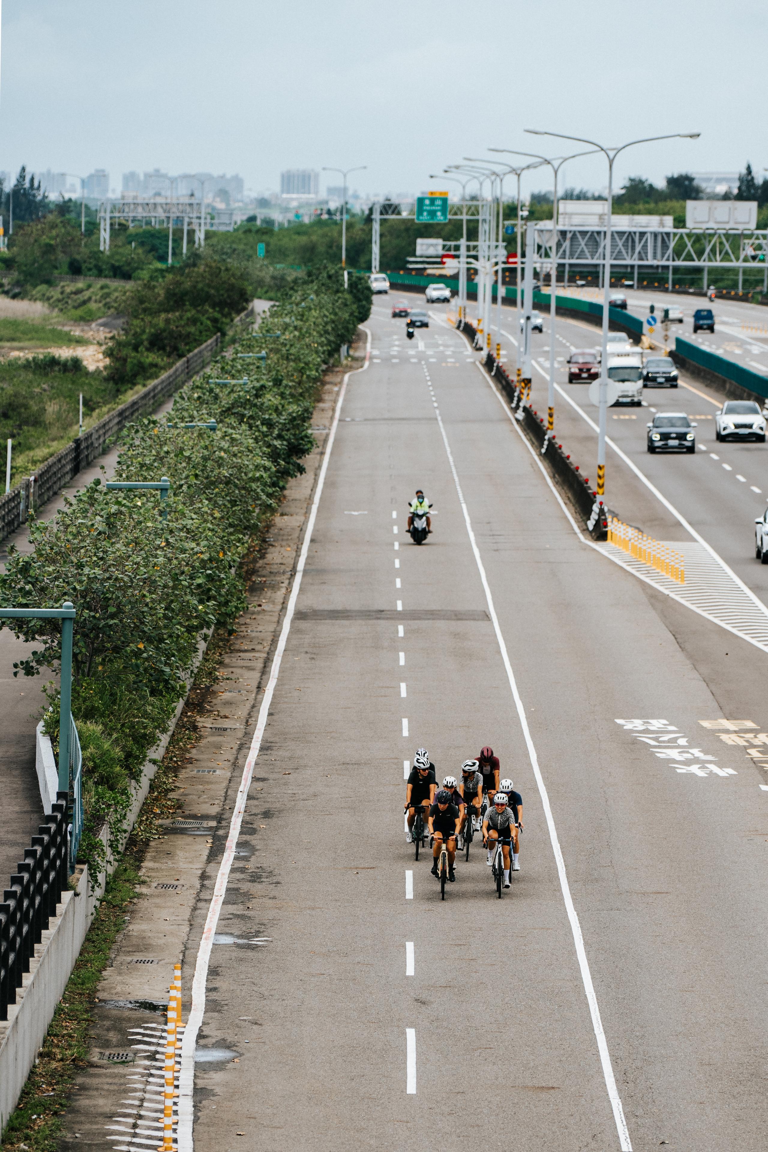 Group of cyclists riding on empty highway lane with cars on adjacent road