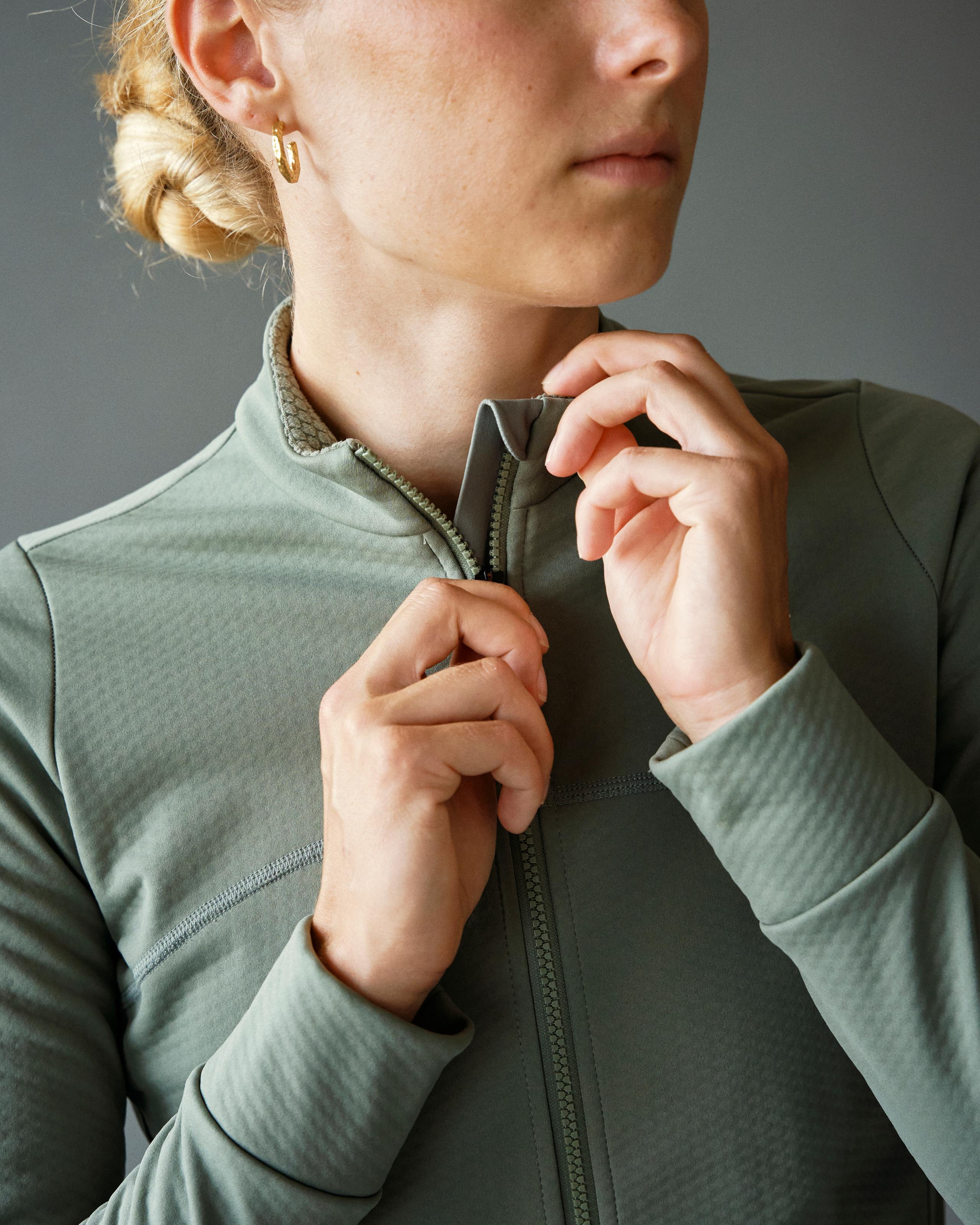 Green Essential Thermal long sleeve cycling jersey on model adjusting front zip with ribbed collar