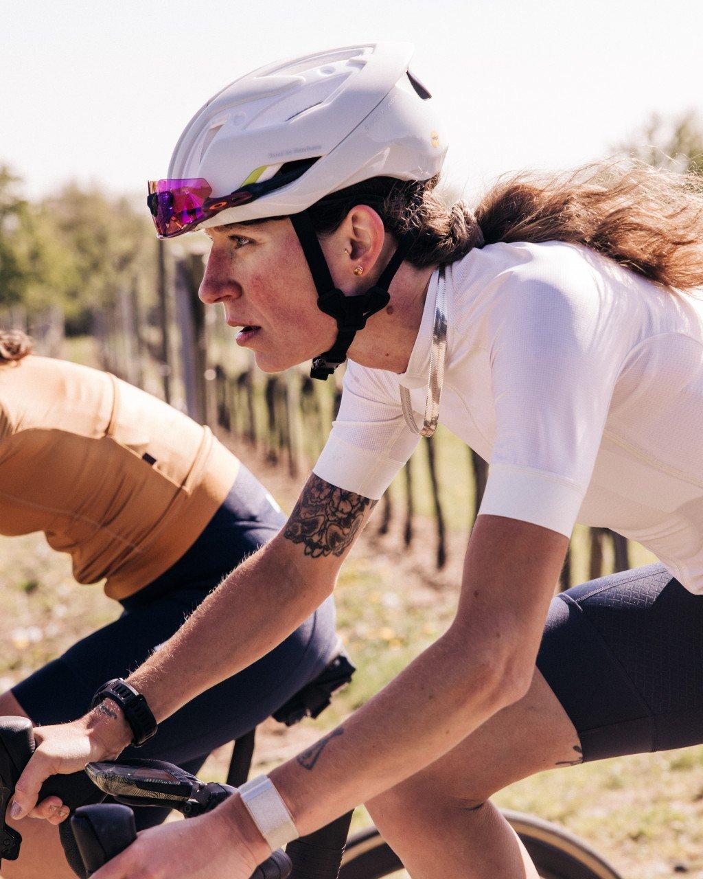 Model wearing white cycling jersey in aerodynamic position on time trial bike with white helmet
