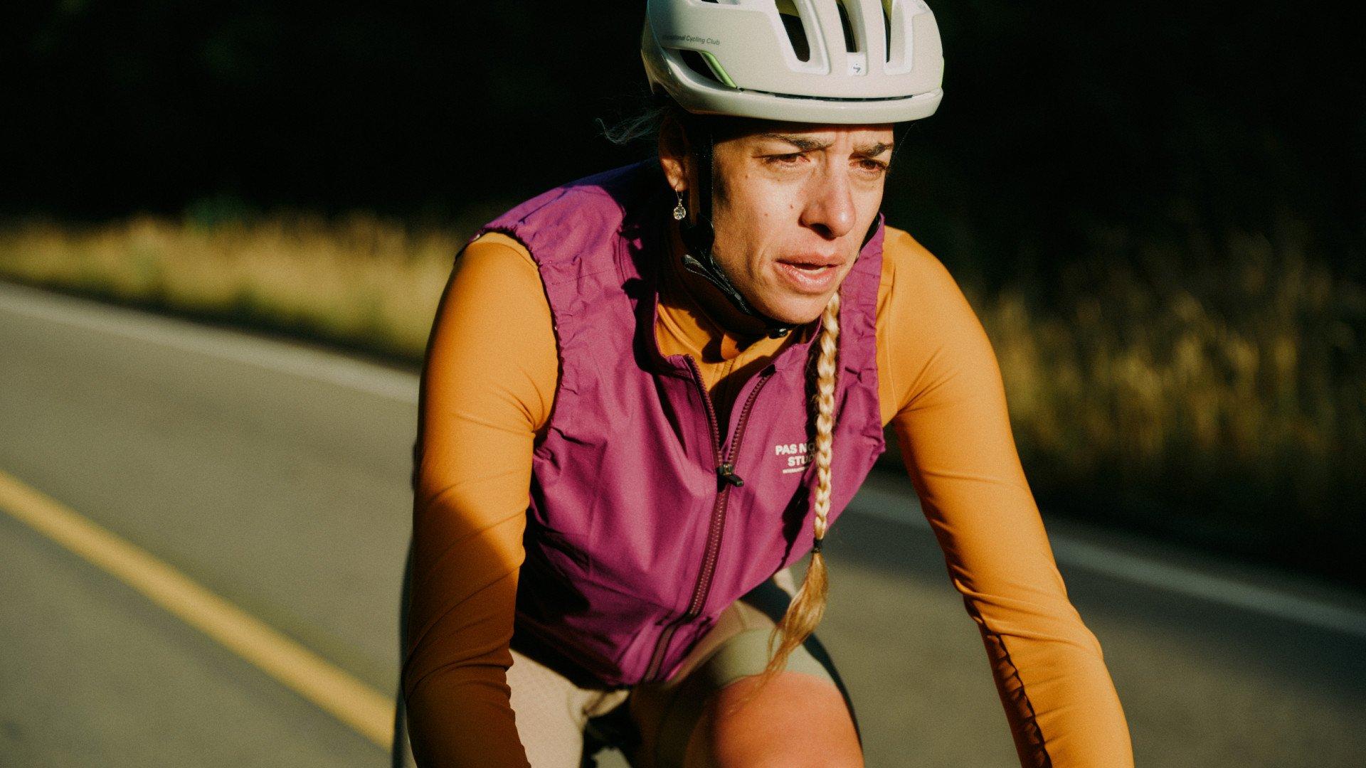 Model wearing purple quilted cycling vest and orange base layer while riding on road