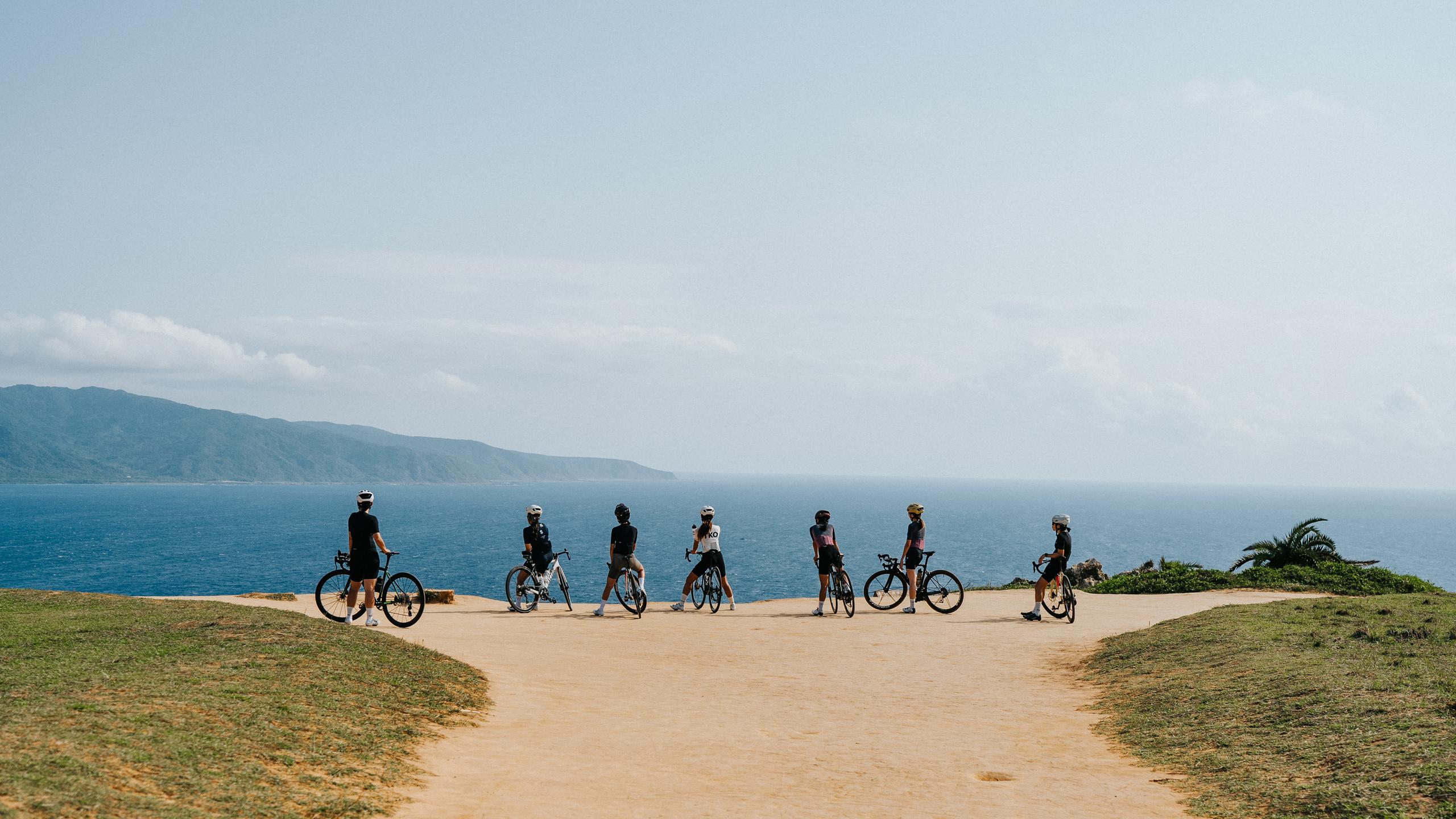 Group of cyclists with bikes standing on coastal path overlooking ocean and mountains