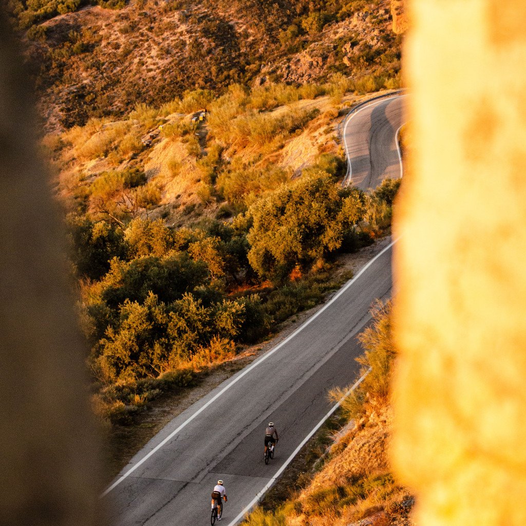 Two cyclists on winding mountain road during golden hour with autumn foliage