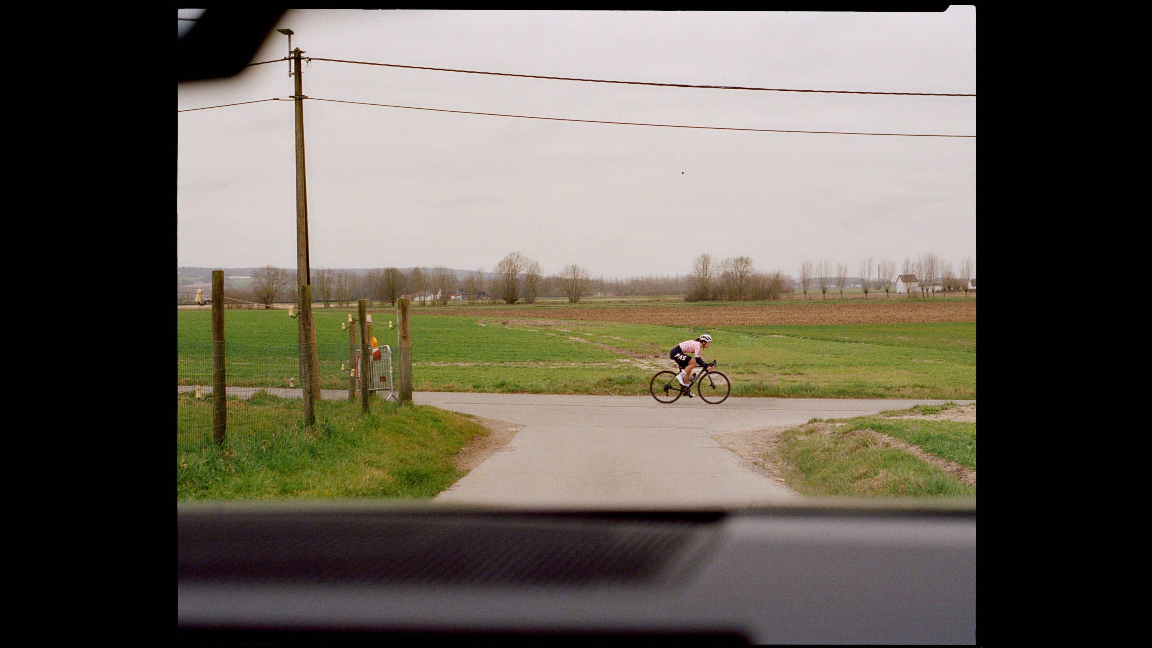 Cyclist in pink jersey riding through rural countryside with green fields and power lines