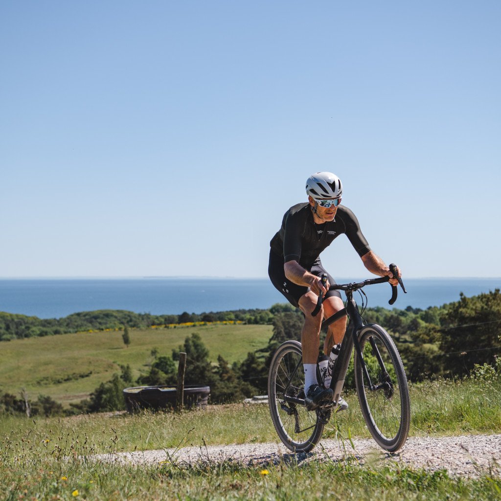 Model wearing black cycling apparel on time trial bike in coastal countryside setting