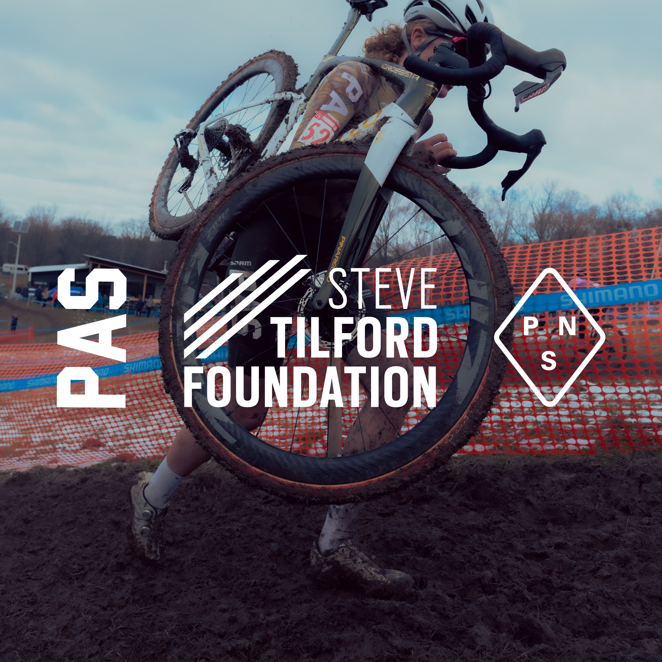 Cyclocross rider carrying bike through muddy course with Steve Tilford Foundation and brand logos