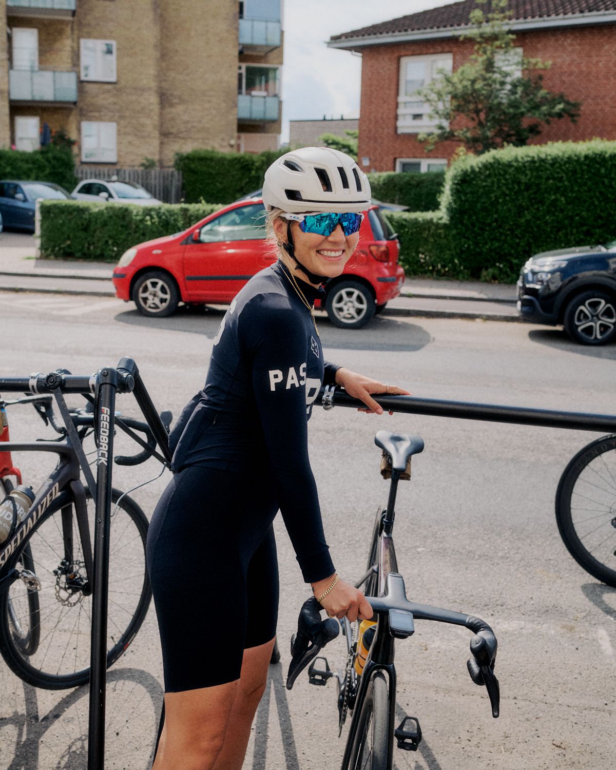 Model wearing navy PAS collection skinsuit with white helmet and blue sunglasses next to time trial bike