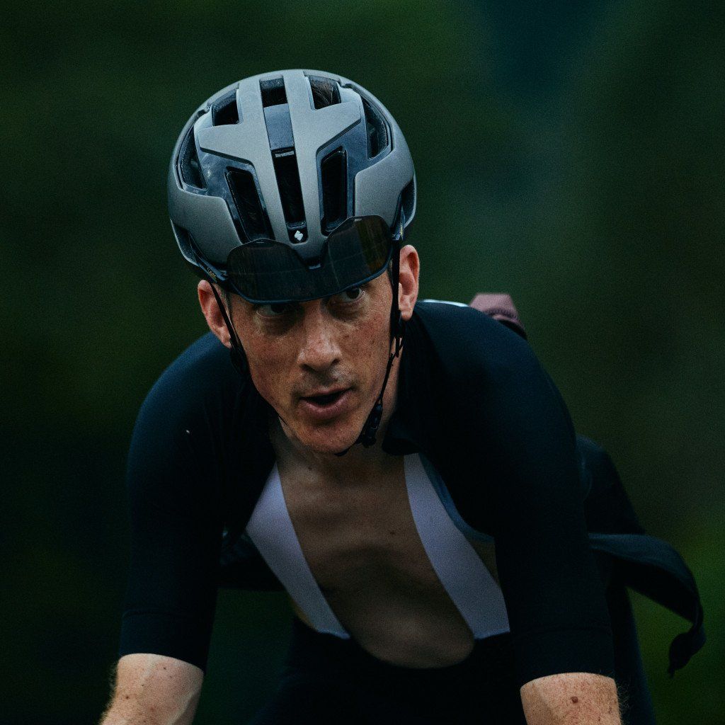 Model wearing grey cycling helmet and black jersey in racing position