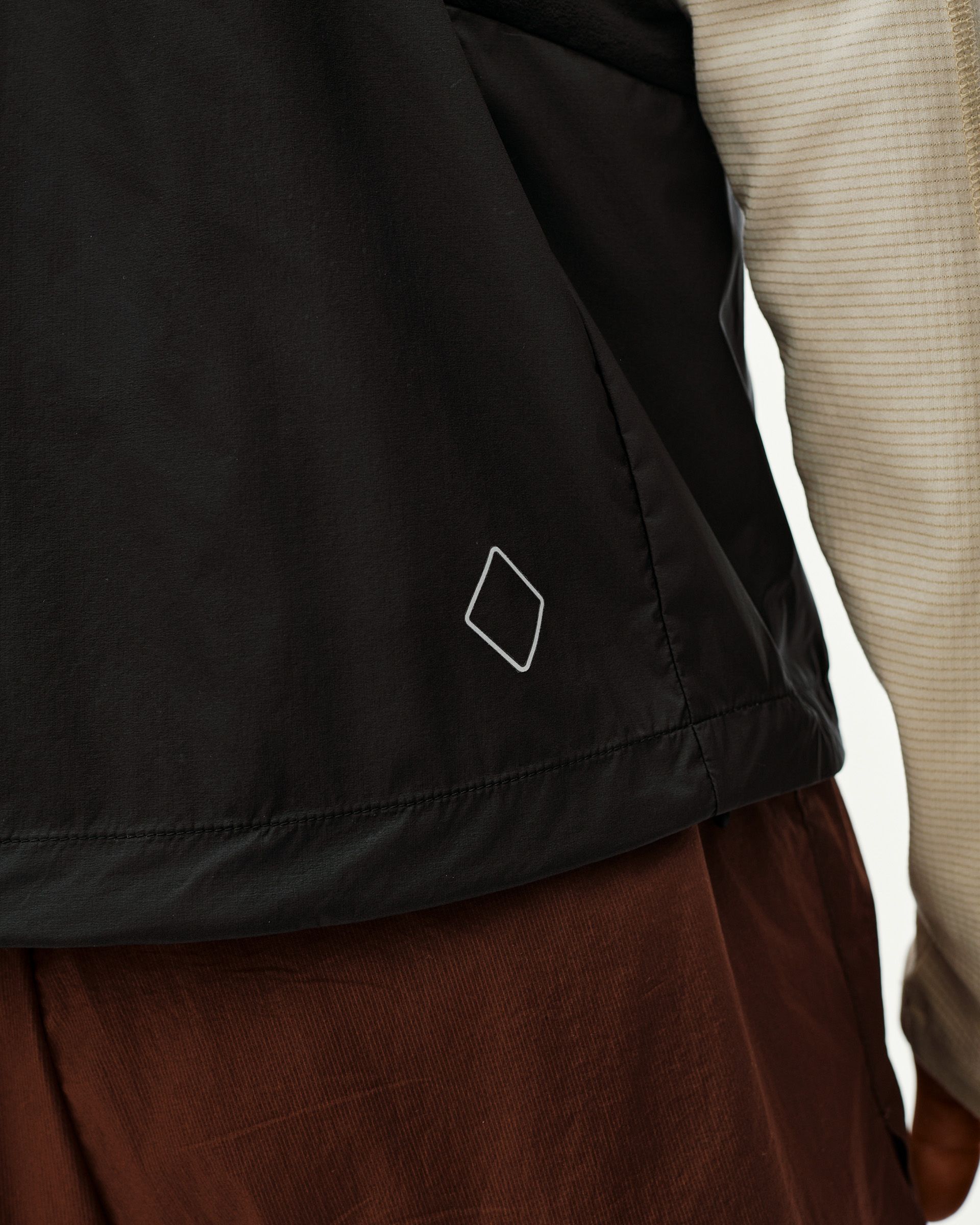 Black Balance Windproof Vest, detail view on model showing diamond logo at hem