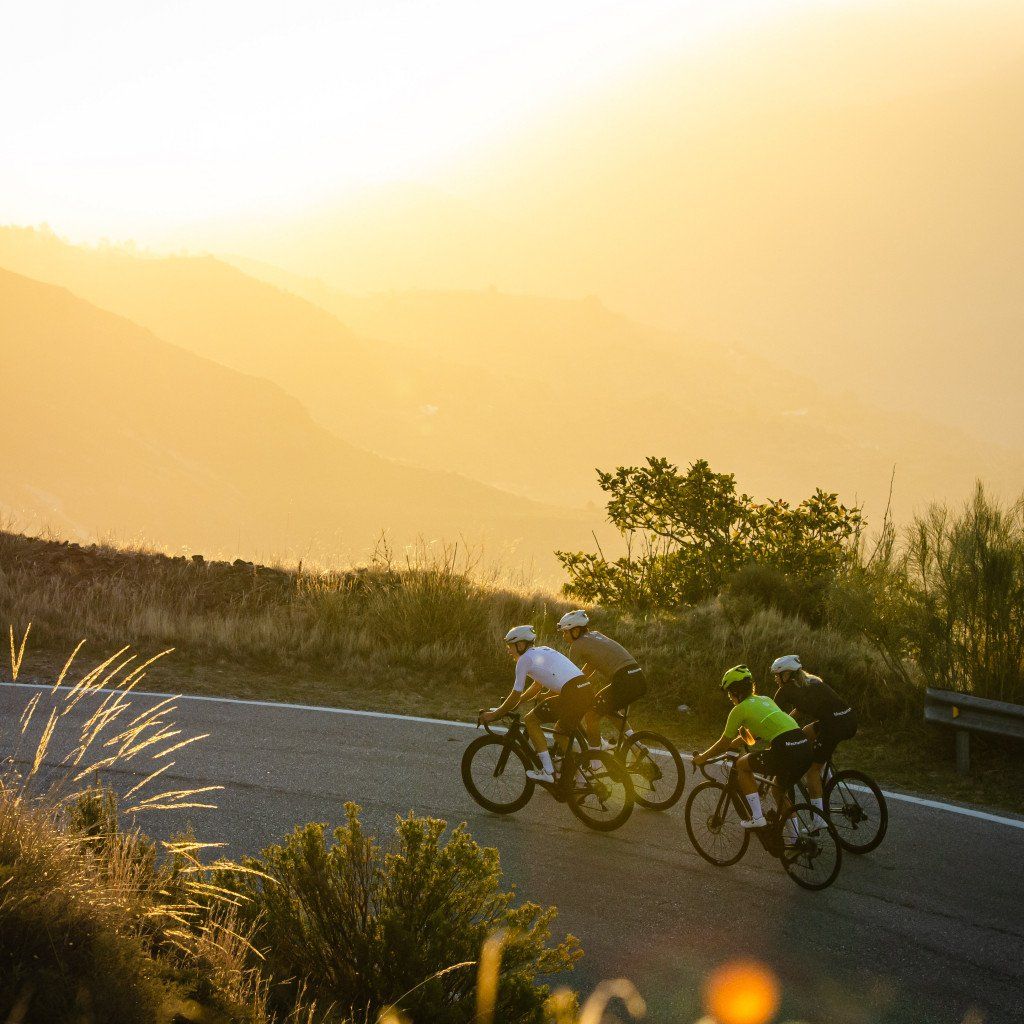 Cyclists in white and green jerseys riding on mountain road during golden hour sunset