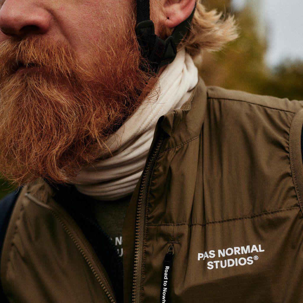 Model wearing olive green zip-up jacket with high collar and chest branding outdoors
