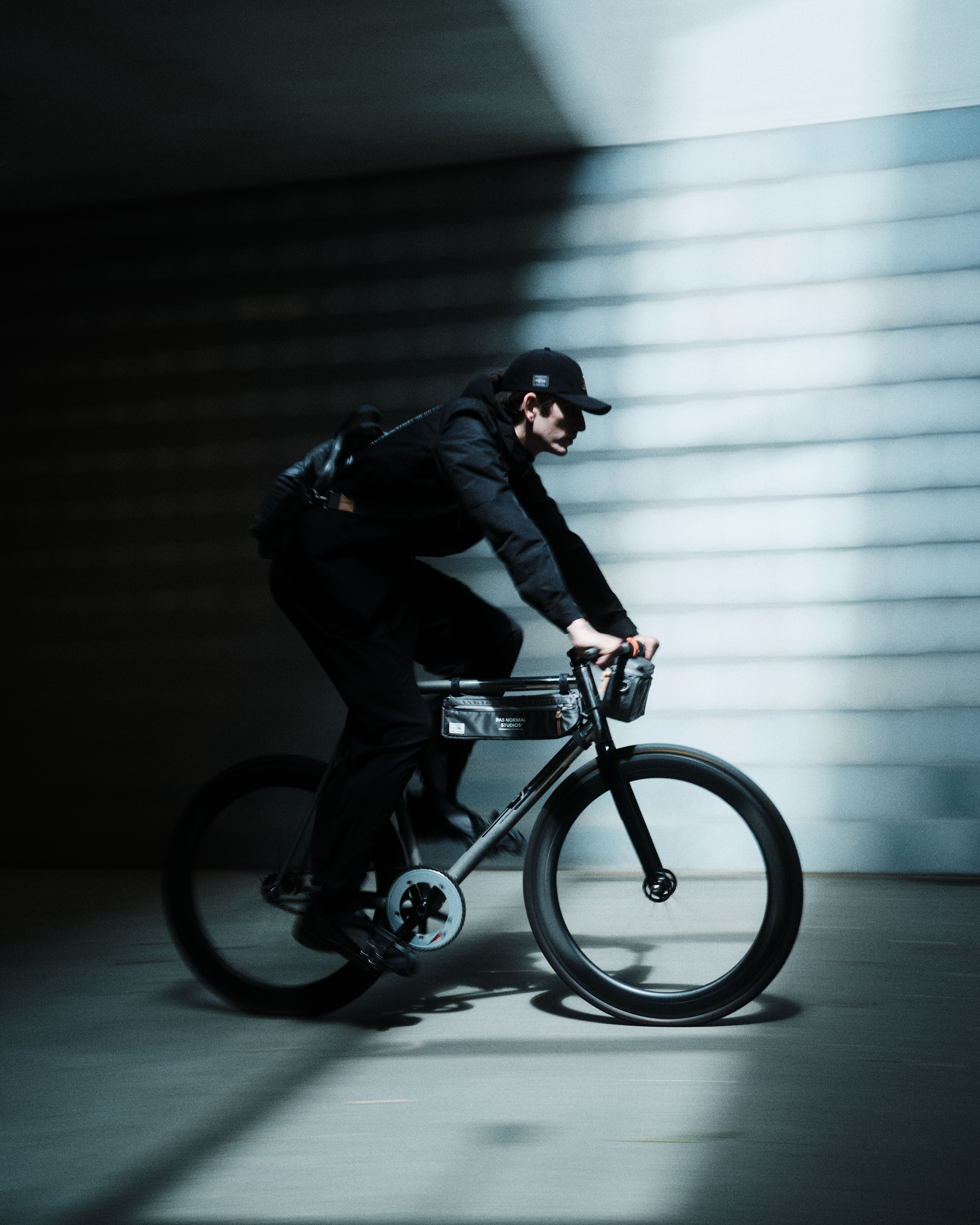 Model wearing black cycling outfit with cap riding bike in urban tunnel with dramatic lighting