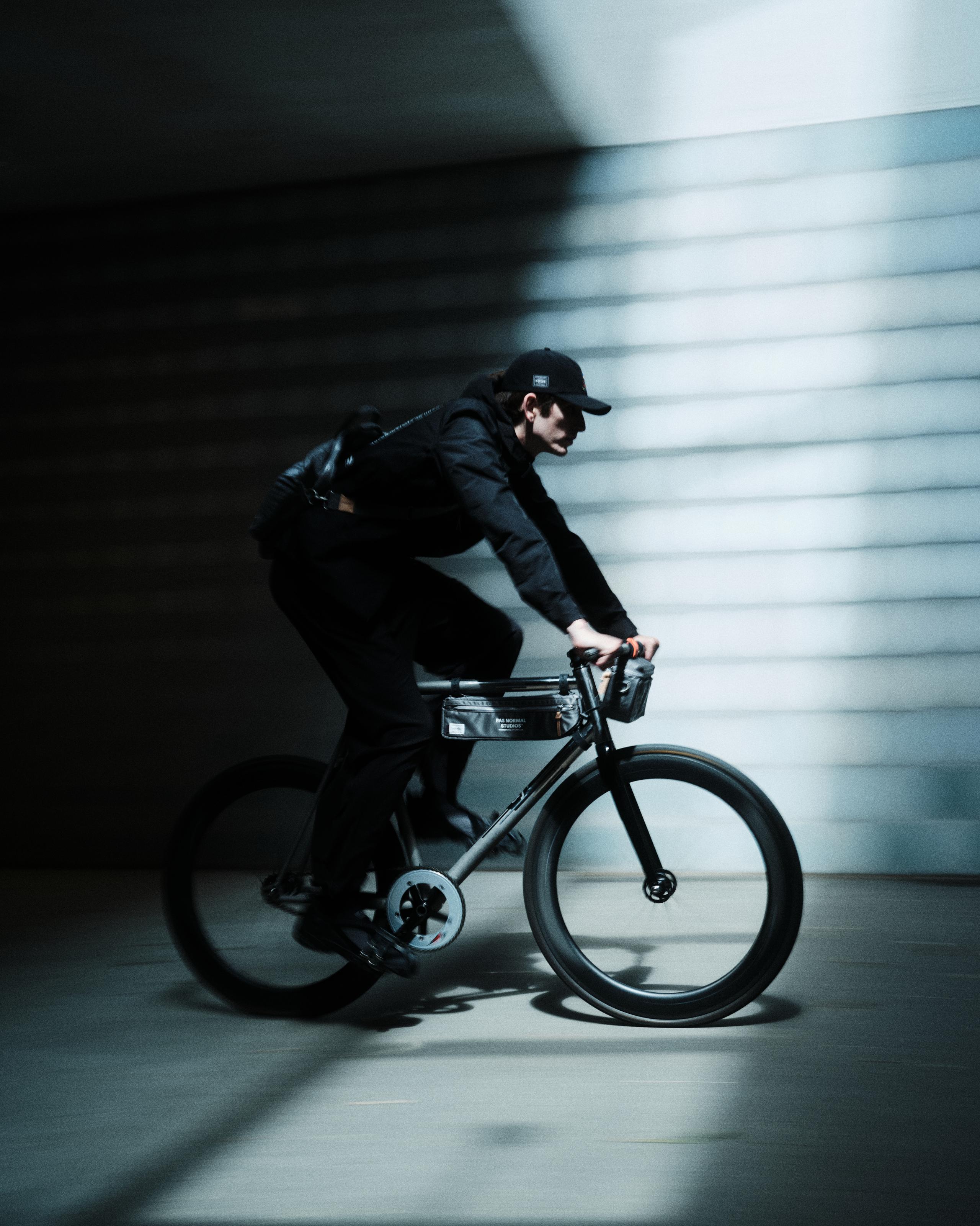 Model wearing black cycling outfit with cap riding bike in urban tunnel with dramatic lighting