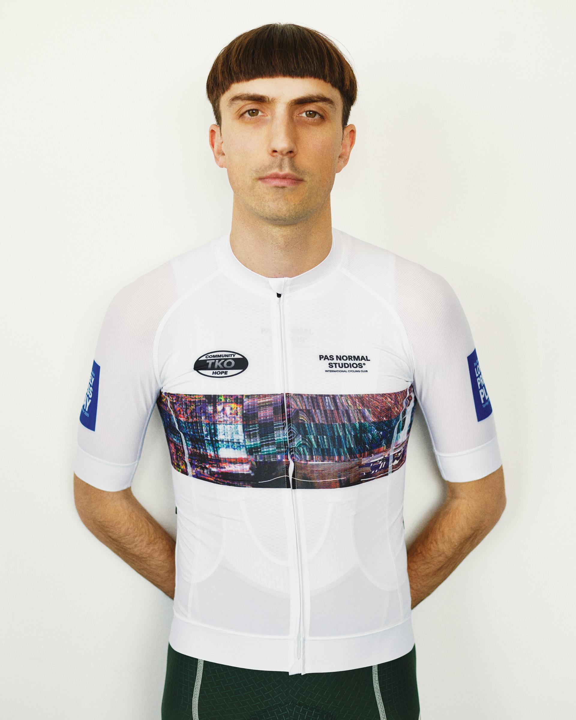 White T.K.O. Mechanism cycling jersey on model, front view with colorful cityscape print band and blue sleeve patches