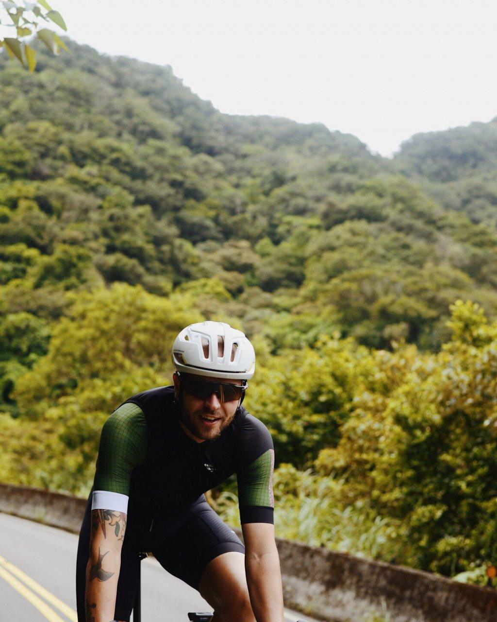 Model wearing cycling jersey with green sleeves and black body on mountain road