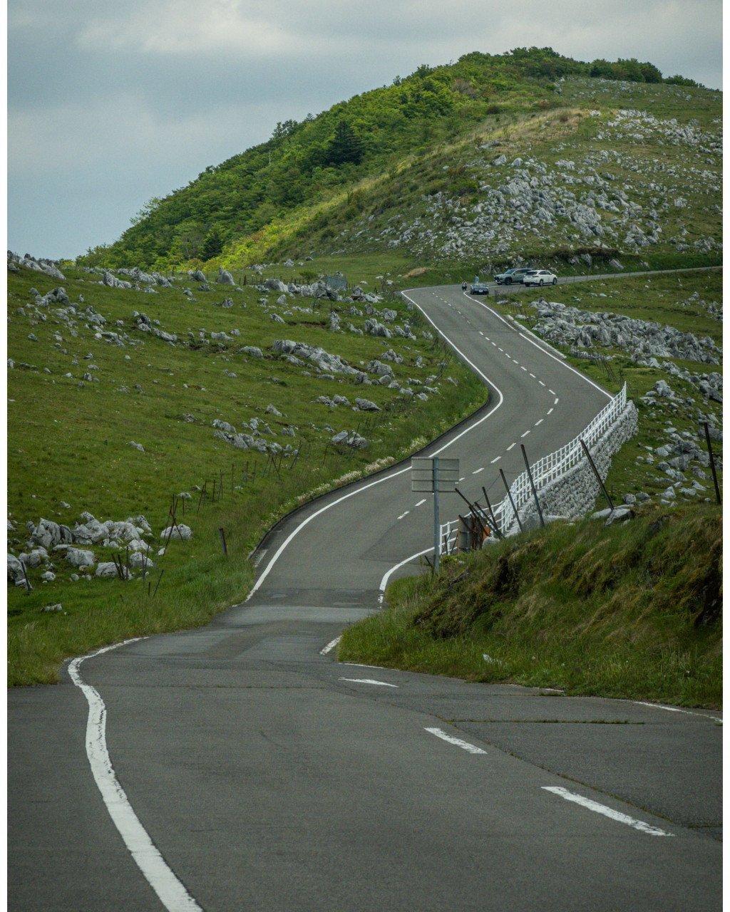 Winding mountain road through green countryside with stone walls and hills