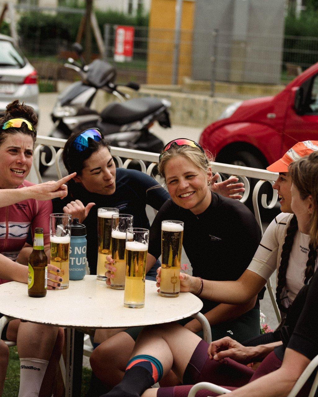 Female cyclists enjoying beers at outdoor cafe table wearing cycling apparel including black jerseys