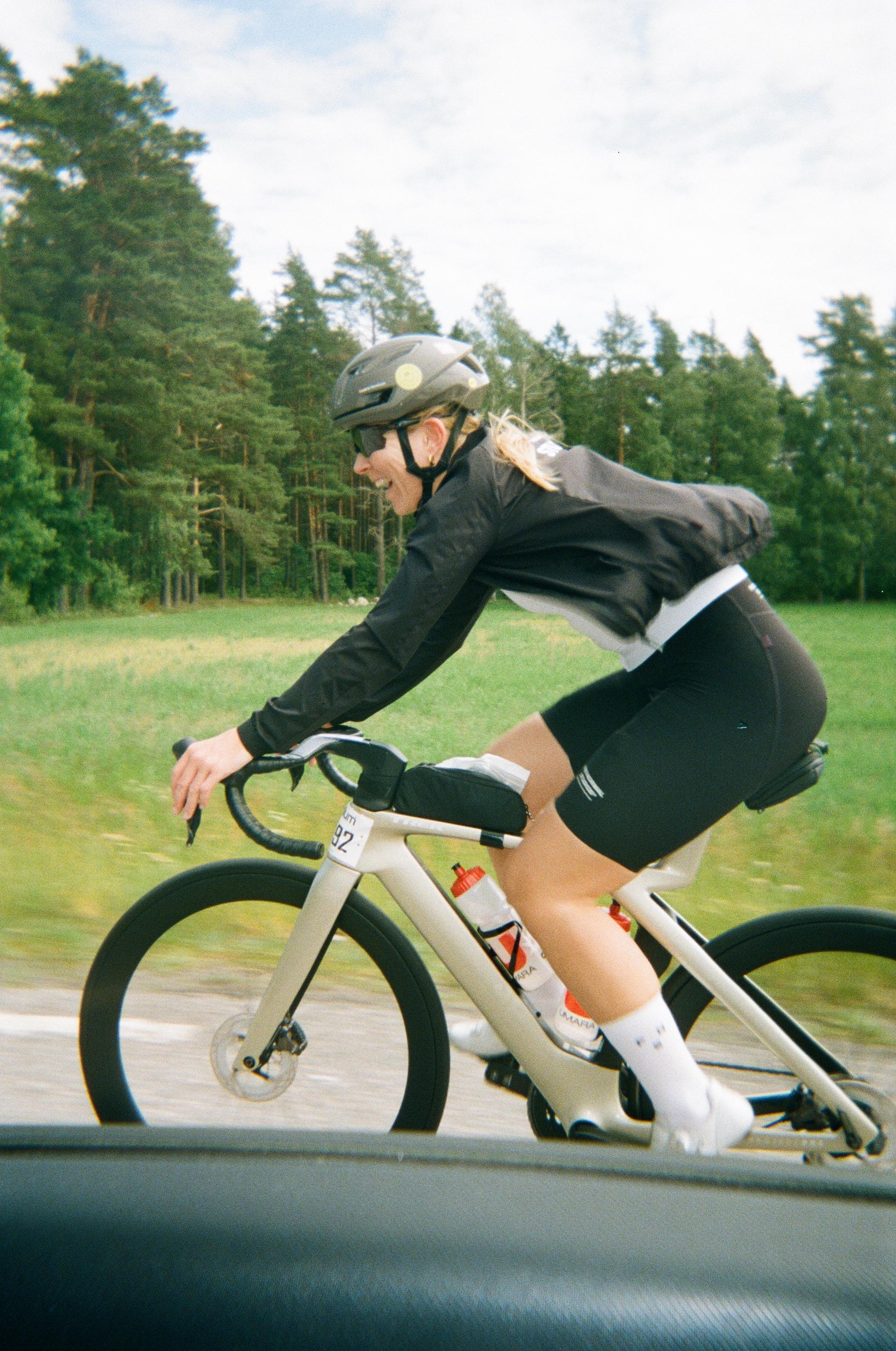Model wearing black cycling kit in aerodynamic position on time trial bike during race