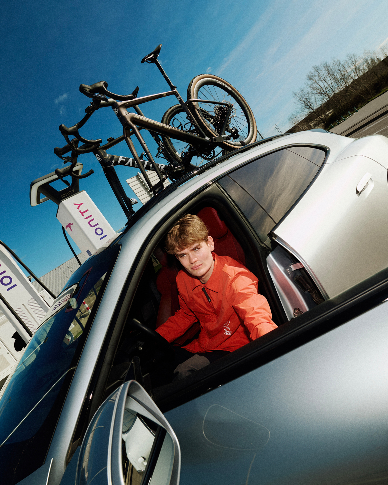 Model wearing red jacket sitting in team car with bicycles on roof rack